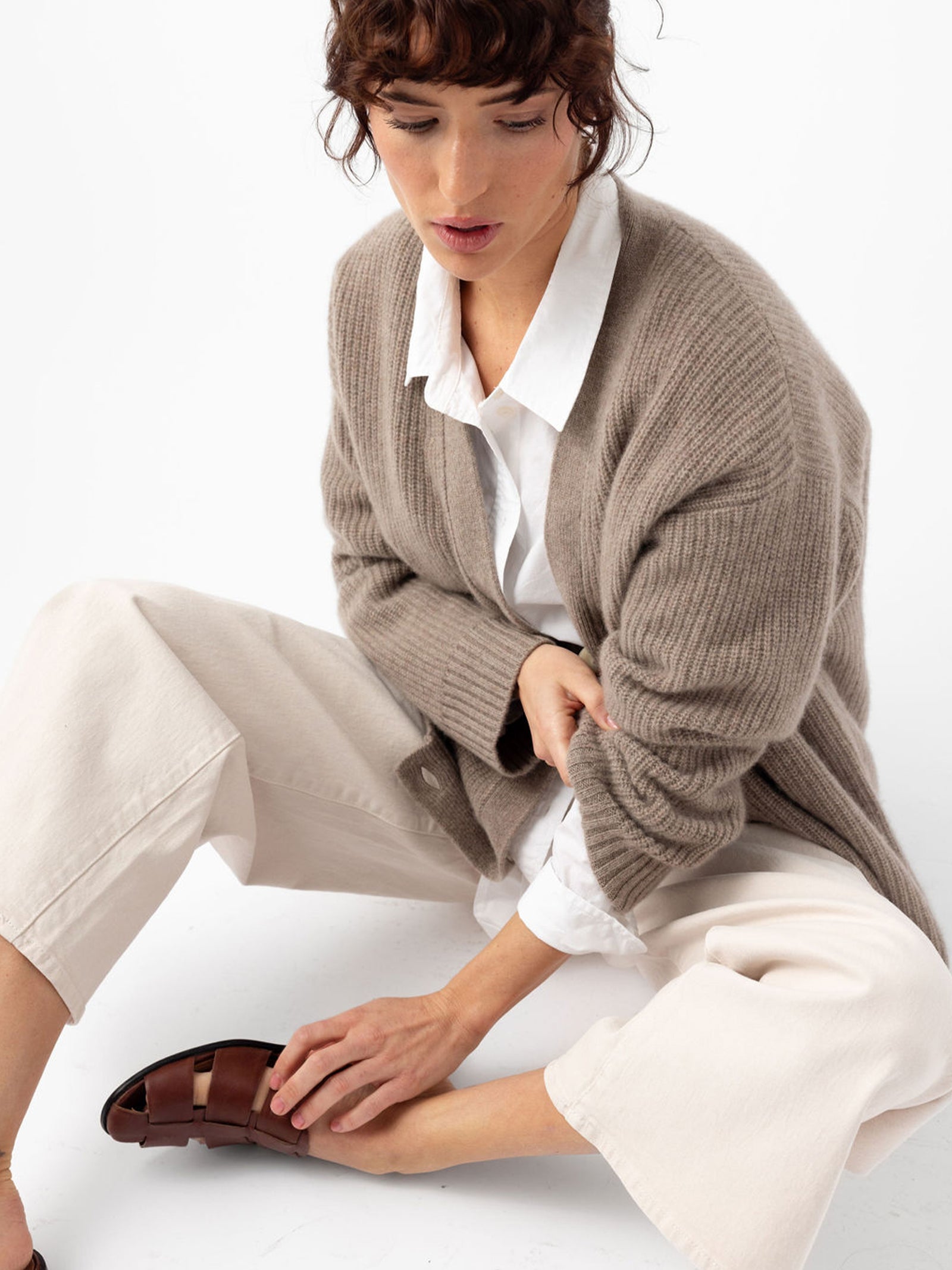 Woman sitting on floor wearing almond sunday cardigan and dress pants 