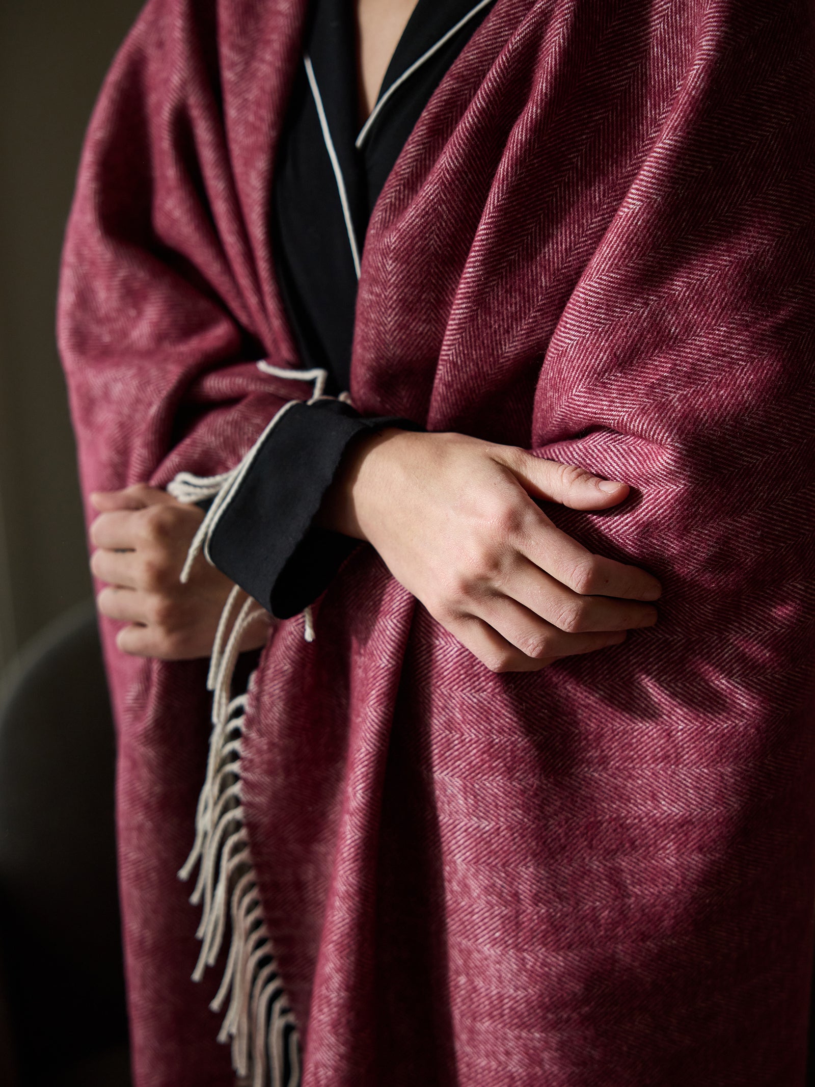 Close up of woman with berry herringbone tassel throw wrapped around her 