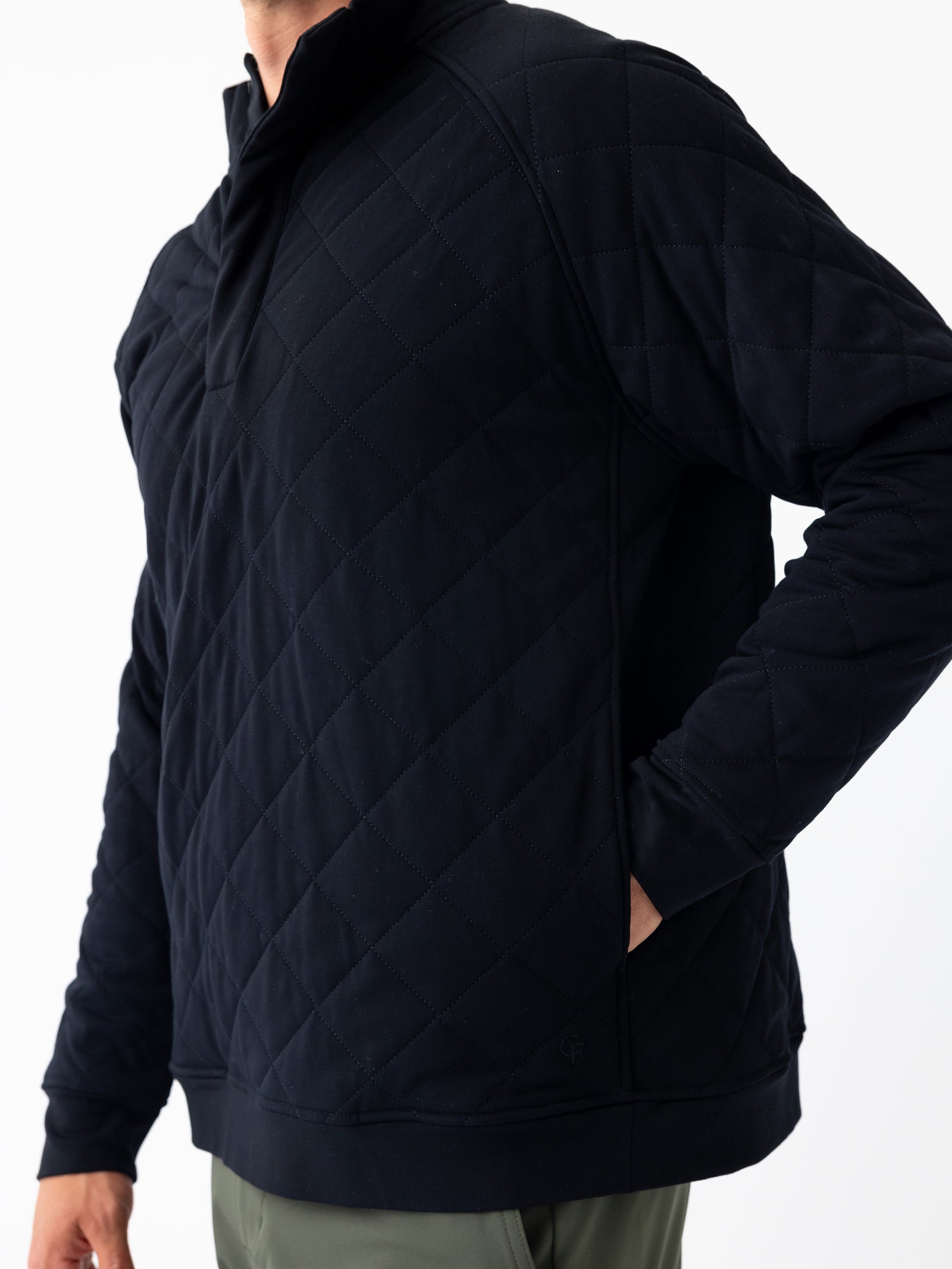 A person wearing Cozy Earth's Men's Ultra-Soft Bamboo Quilted Snap Pullover, featuring a high collar and long sleeves in a black, quilted design, stands with one hand in their pocket. The torso and partial arm of the individual are visible against a plain white background. 