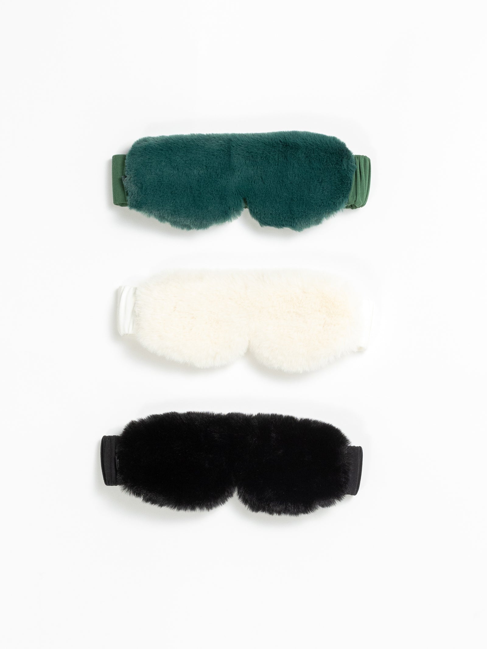 The Cozy Earth Faux Fur Sleep Masks in Jade, Ivory, and Black are pictured on a white background. 