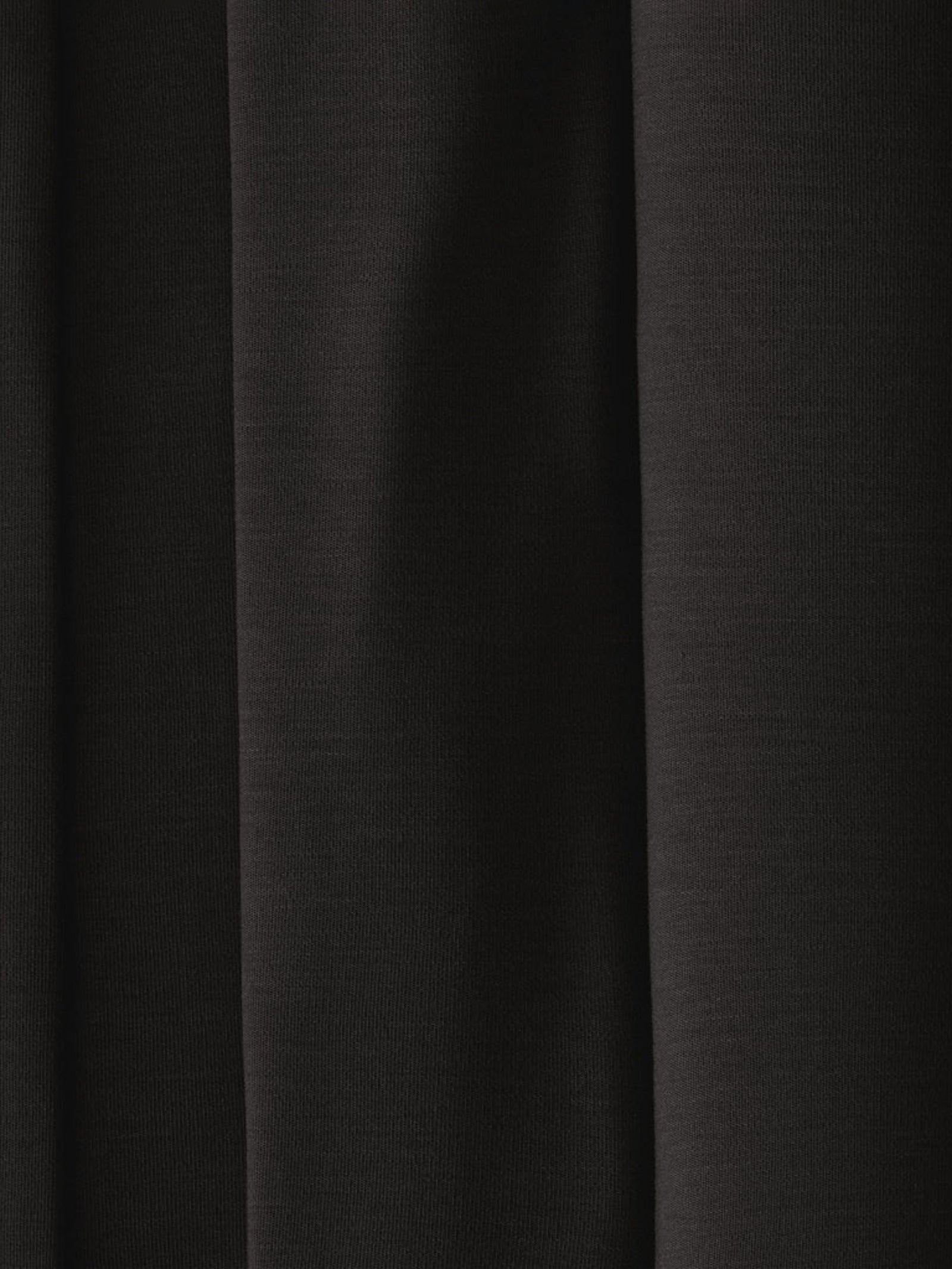 A close-up of the dark black fabric from the Men's Stretch-Knit Short Sleeve Bamboo Pajama Set by Cozy Earth showcases subtle vertical folds that contribute to its textured appearance. The fabric appears opaque and smooth, with soft shadows highlighting the folds.