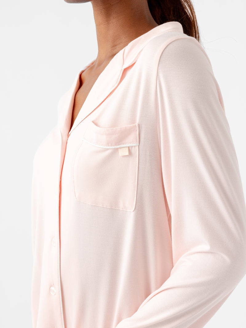 A person is wearing the Women's Long Sleeve Bamboo Pajama Top in Stretch-Knit TALL from HIDE. The light pink shirt features a collar, a chest pocket, and a visible button-down design. The plain white background highlights the intricate details of the top.