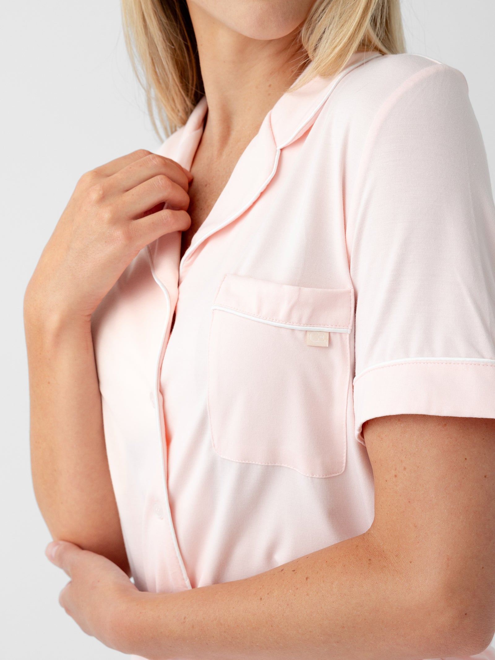 Close-up of a person wearing the Women's Short Sleeve Bamboo Pajama Top in Stretch-Knit by HIDE. They are holding the collar with one hand and have a small pocket on the chest. The background is plain white. 