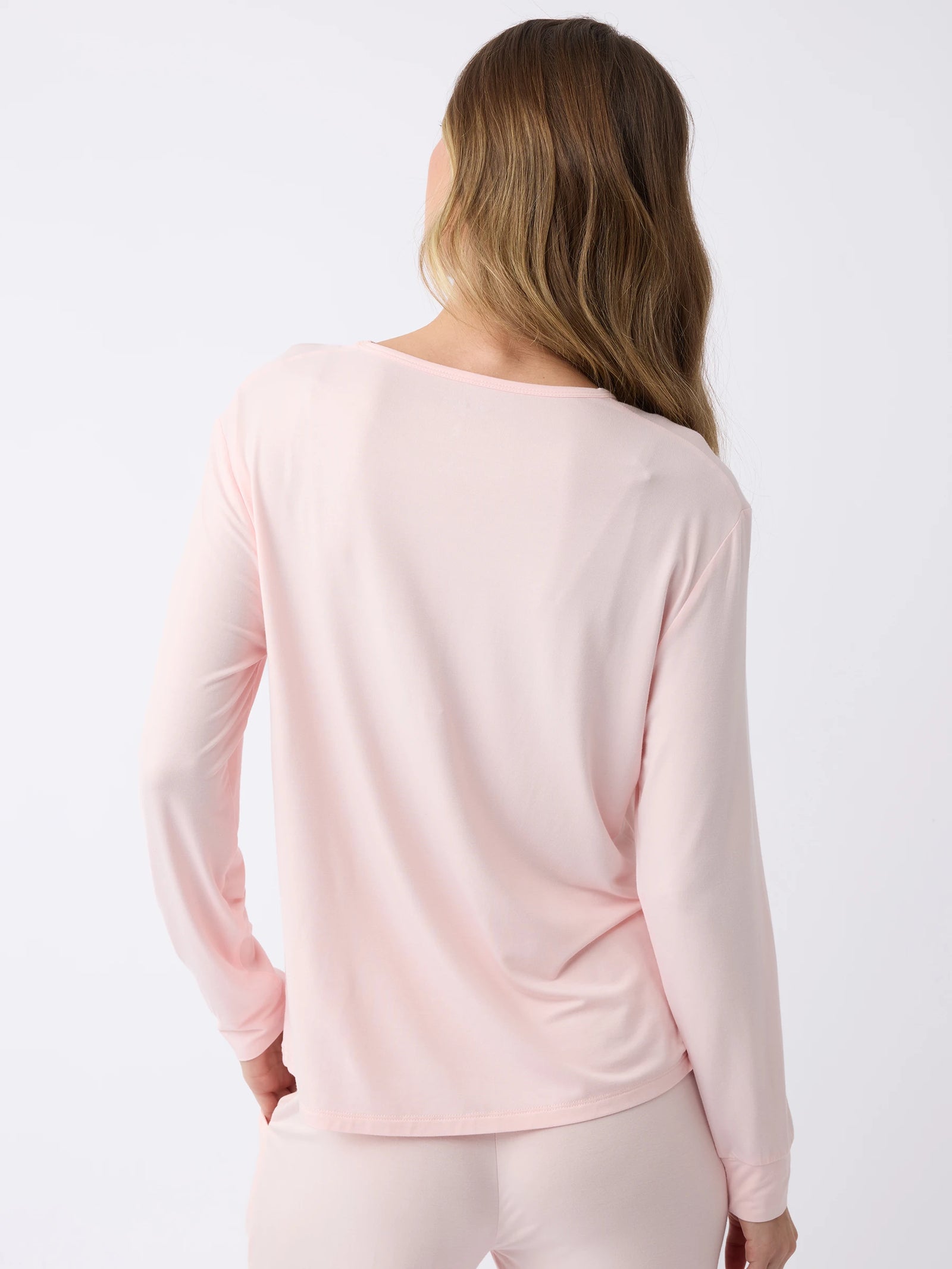 Against a simple white background, a person with long hair models the back of the Women's Stretch Knit Bamboo Long Sleeve Lounge Tee by Cozy Earth in light pink. 