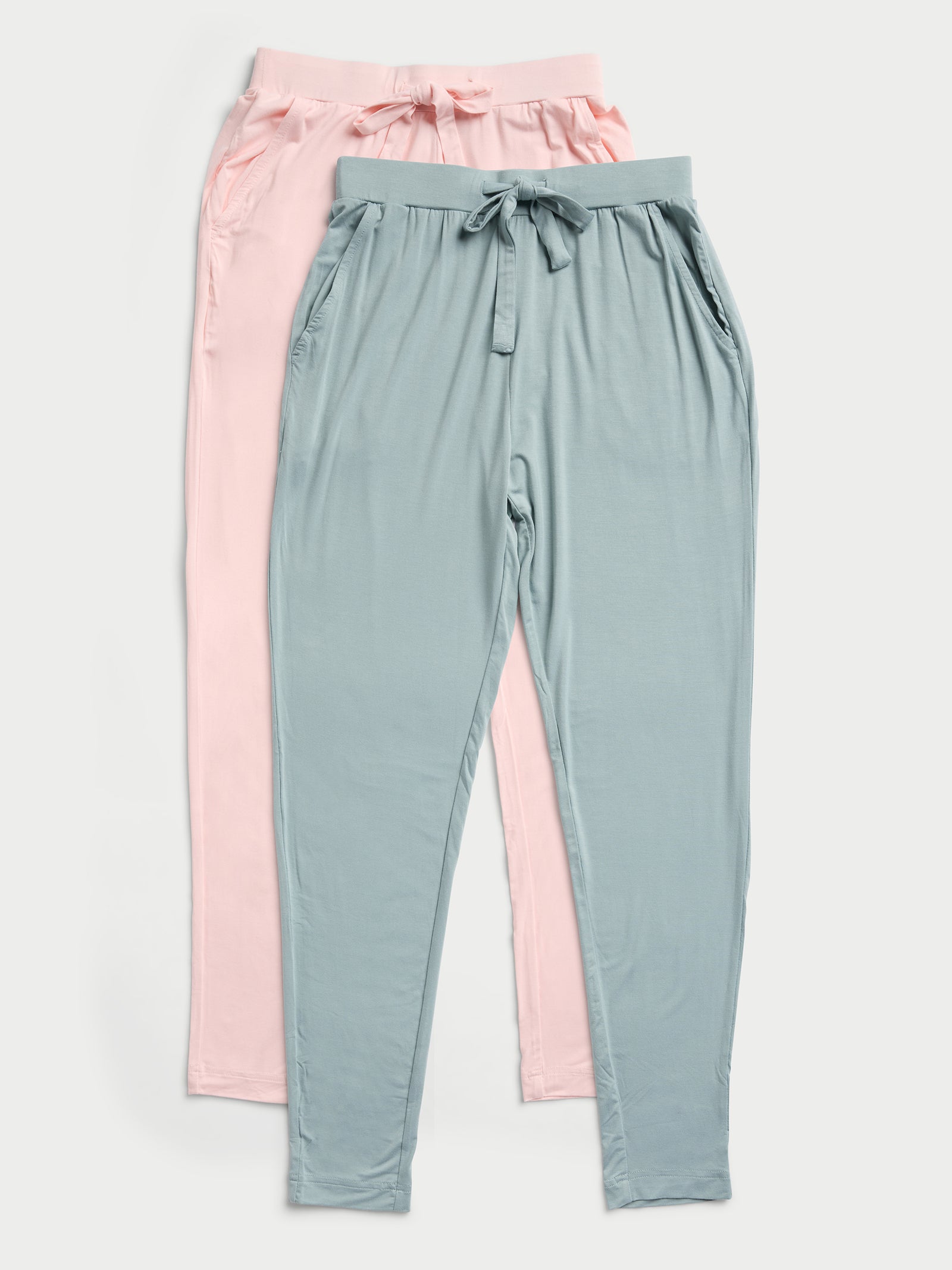 Two pairs of Cozy Earth's Stretch Knit Bamboo Tapered Pants are laid flat. One pair is in light pink and the other in muted teal. Both feature elastic waistbands and side pockets, set against a plain background. 