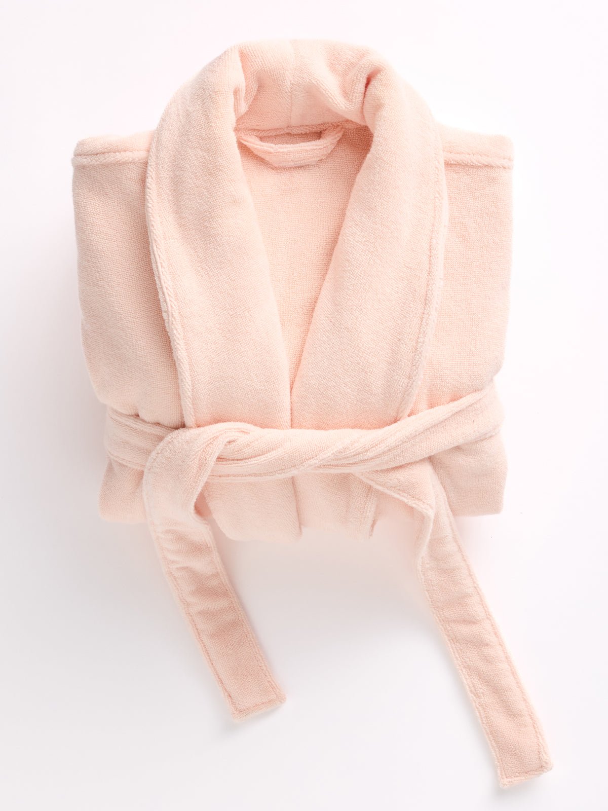 A Luxe Bath Robe from Cozy Earth, in folded pink, features a soft plush texture with a loosely tied belt at the front, all set against a white background. 