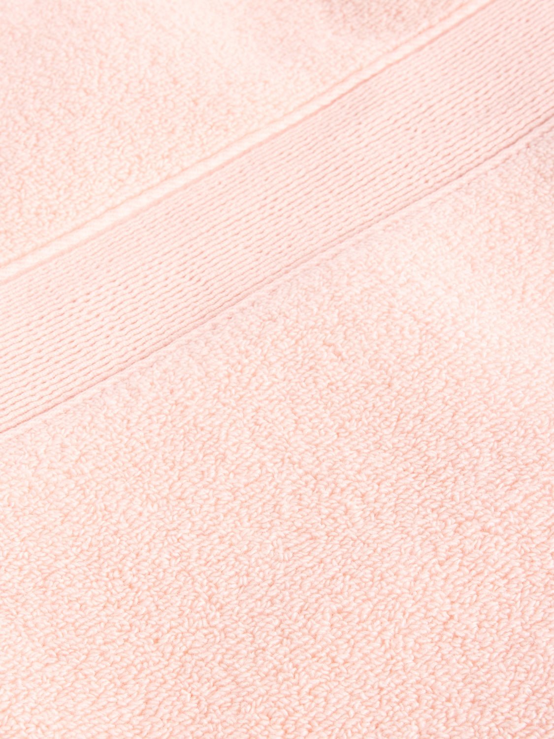 Close-up of a Luxe Bath Towel by Cozy Earth in light pink, featuring a fluffy texture with a horizontal band design near the top edge. 