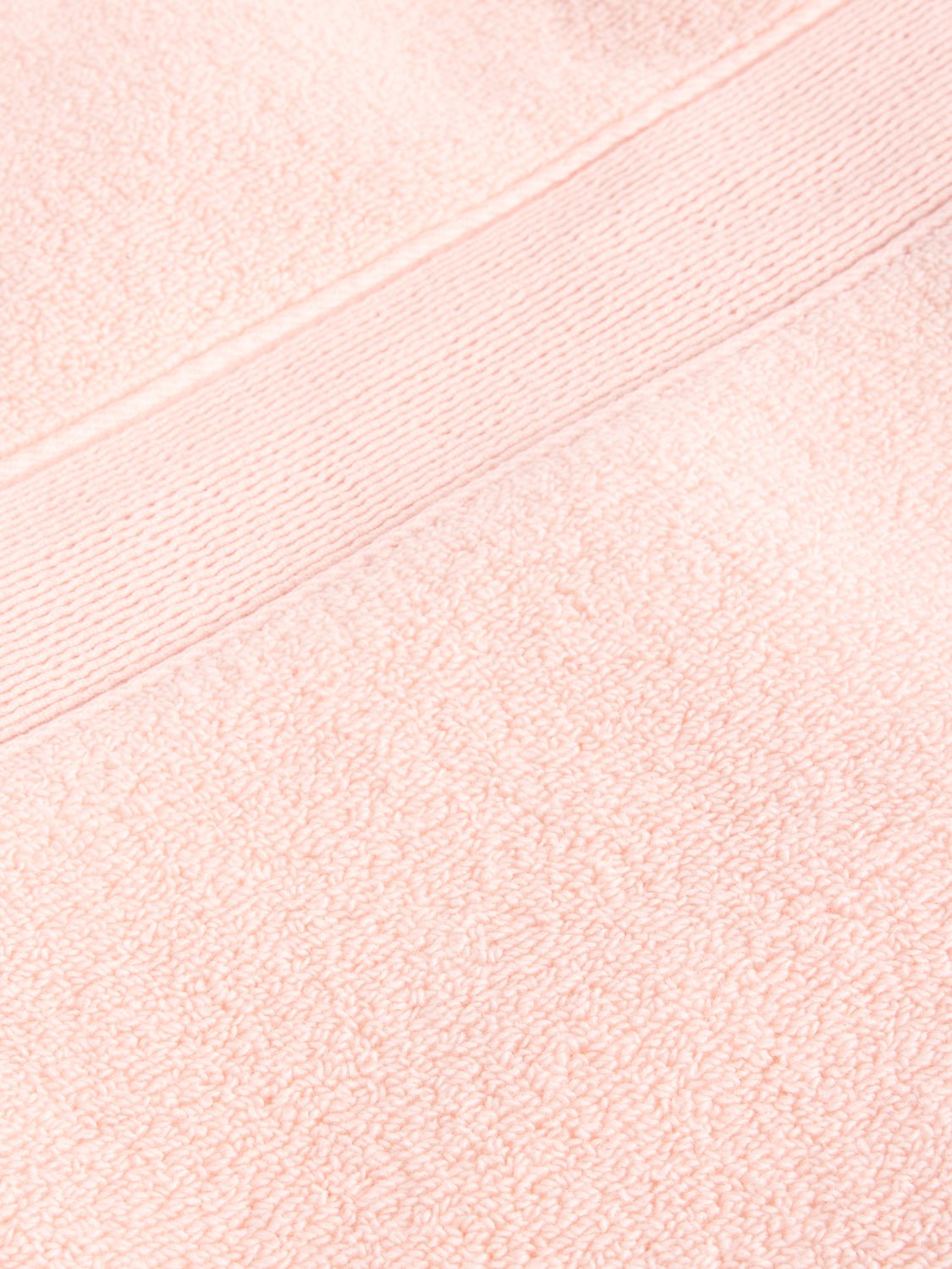 Close-up of a Luxe Bath Towel by Cozy Earth in light pink, featuring a fluffy texture with a horizontal band design near the top edge. 