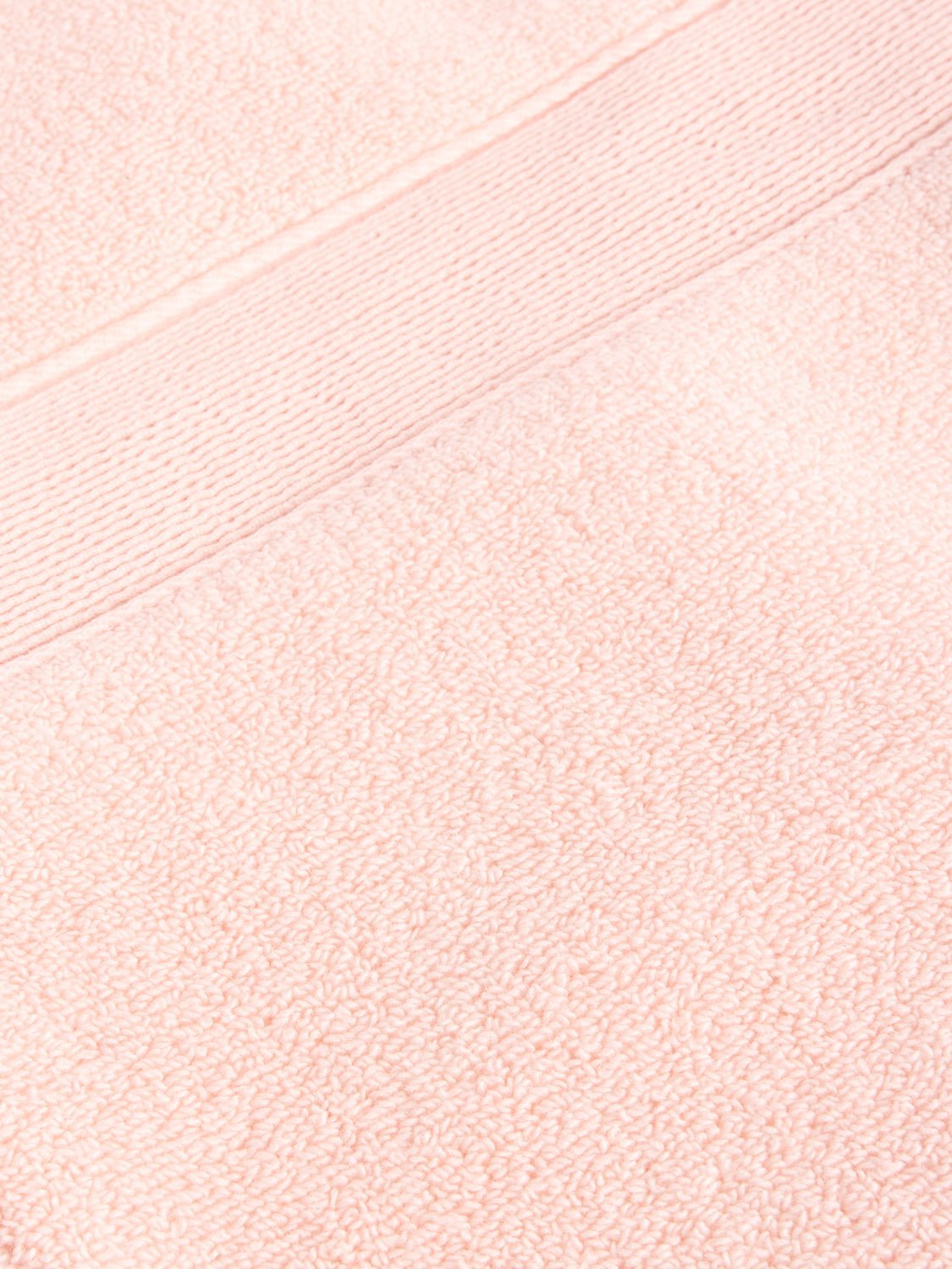 A close-up of a Luxe Washcloth by Cozy Earth reveals the textured fabric in soft, pastel pink, featuring a smooth horizontal band with a fine line pattern running across it. 