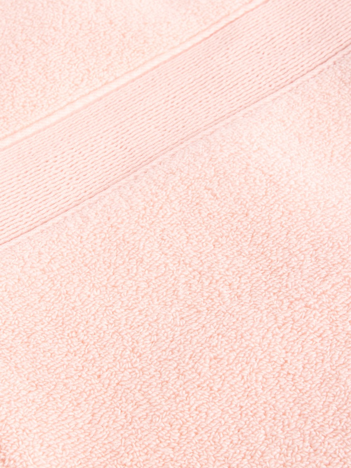 A close-up of a Luxe Washcloth by Cozy Earth reveals the textured fabric in soft, pastel pink, featuring a smooth horizontal band with a fine line pattern running across it. 