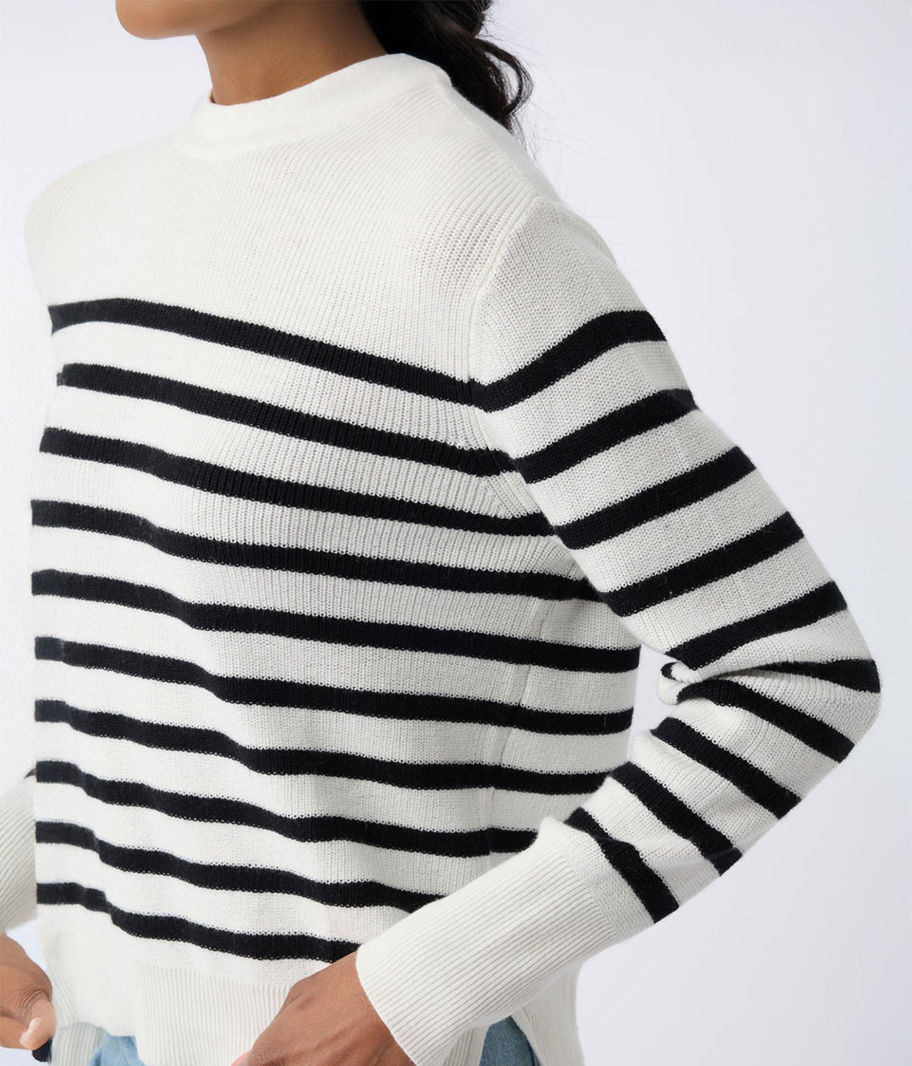 A person wearing Cozy Earth's Women's Rowan Sweater, featuring black horizontal stripes on a white background, stands against a plain backdrop. Their face remains unseen in the photo. 