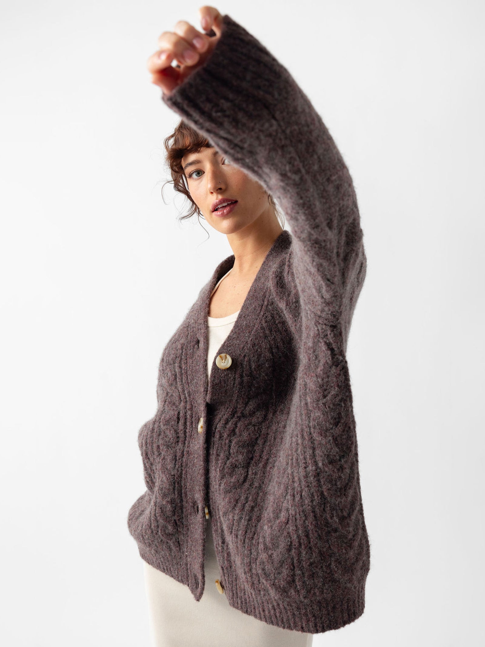 Studio image of woman wearing bordeaux cardigan holding her left arm toward the camera 