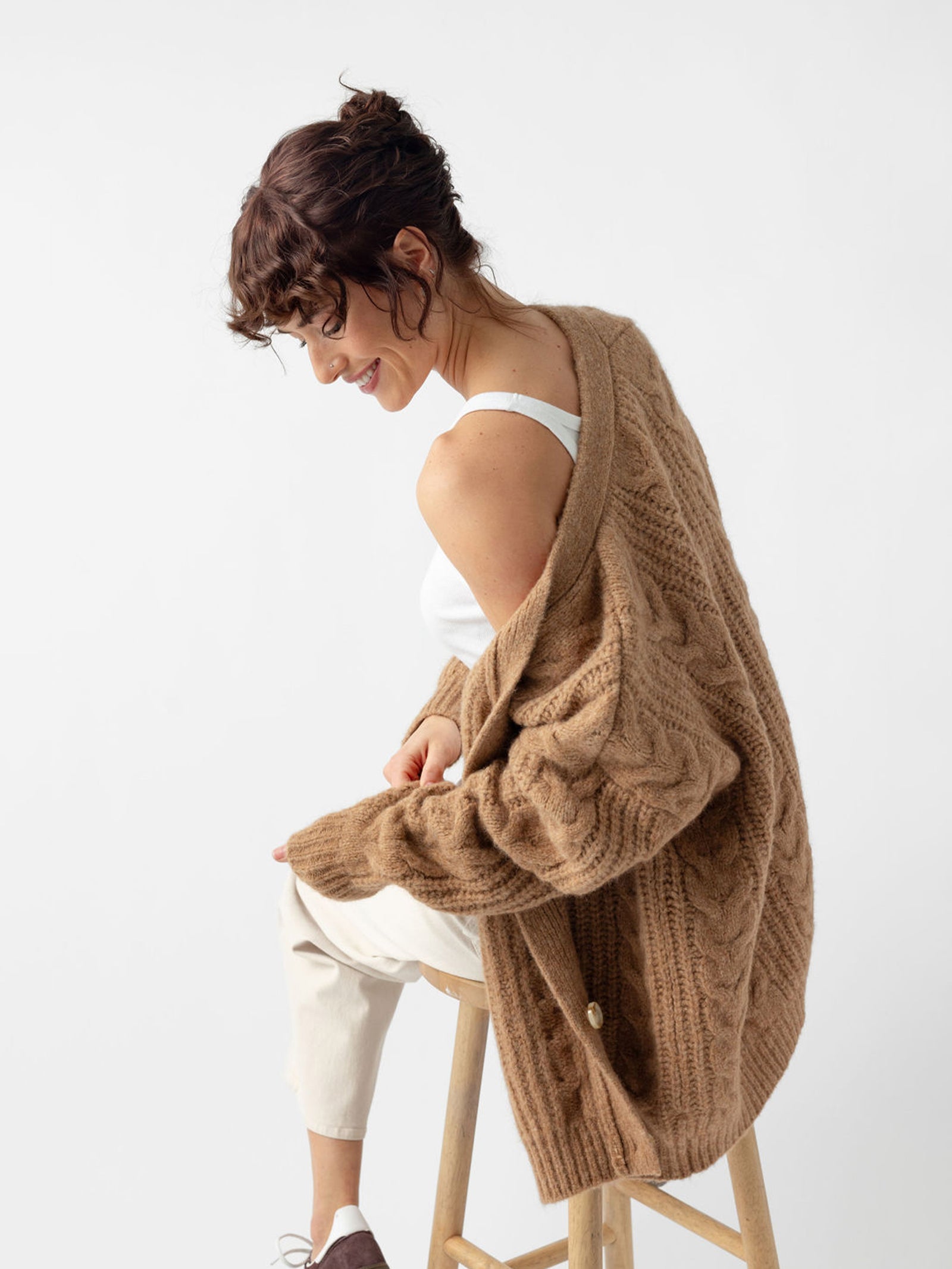 Woman sitting on wooden stool wearing camel cardigan off the shoulder 