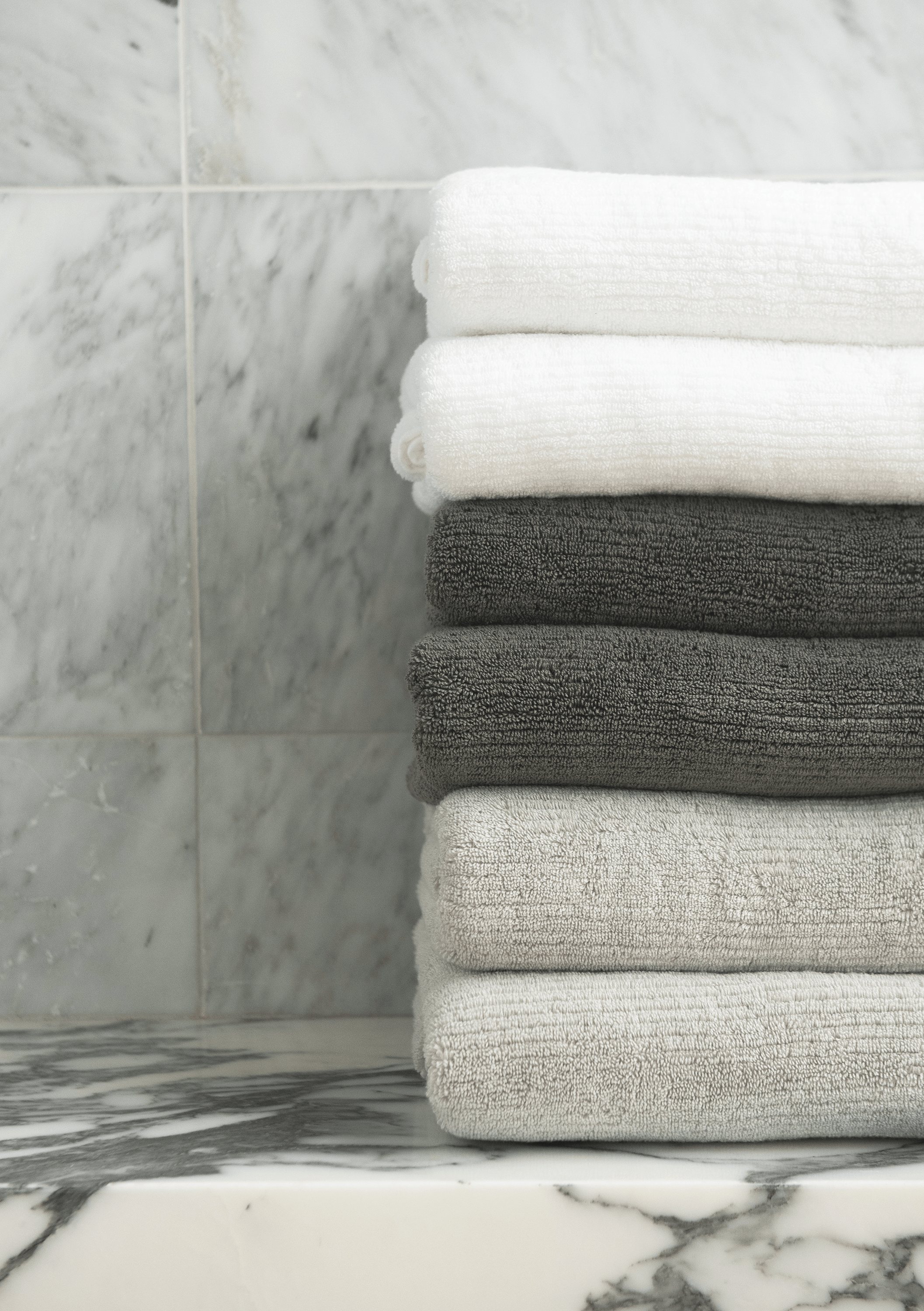 Ribbed Terry Hand Towel in the colors Light Grey, Charcoal, and White. Photo of Ribbed Terry Hand Towel taken with the Ribbed Terry Hand Towel resting on a bathroom sink.