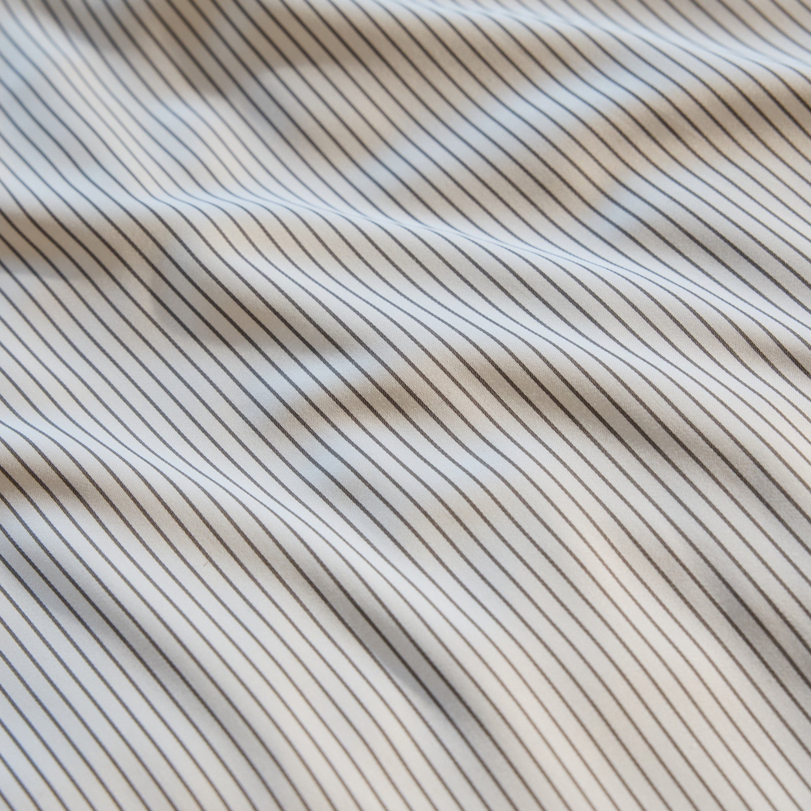 A close-up of the Bamboo Fitted Sheet by Cozy Earth showcases a pattern of thin, evenly spaced vertical black stripes on a white background. The sheet appears slightly wrinkled, creating a series of soft waves across its surface. 