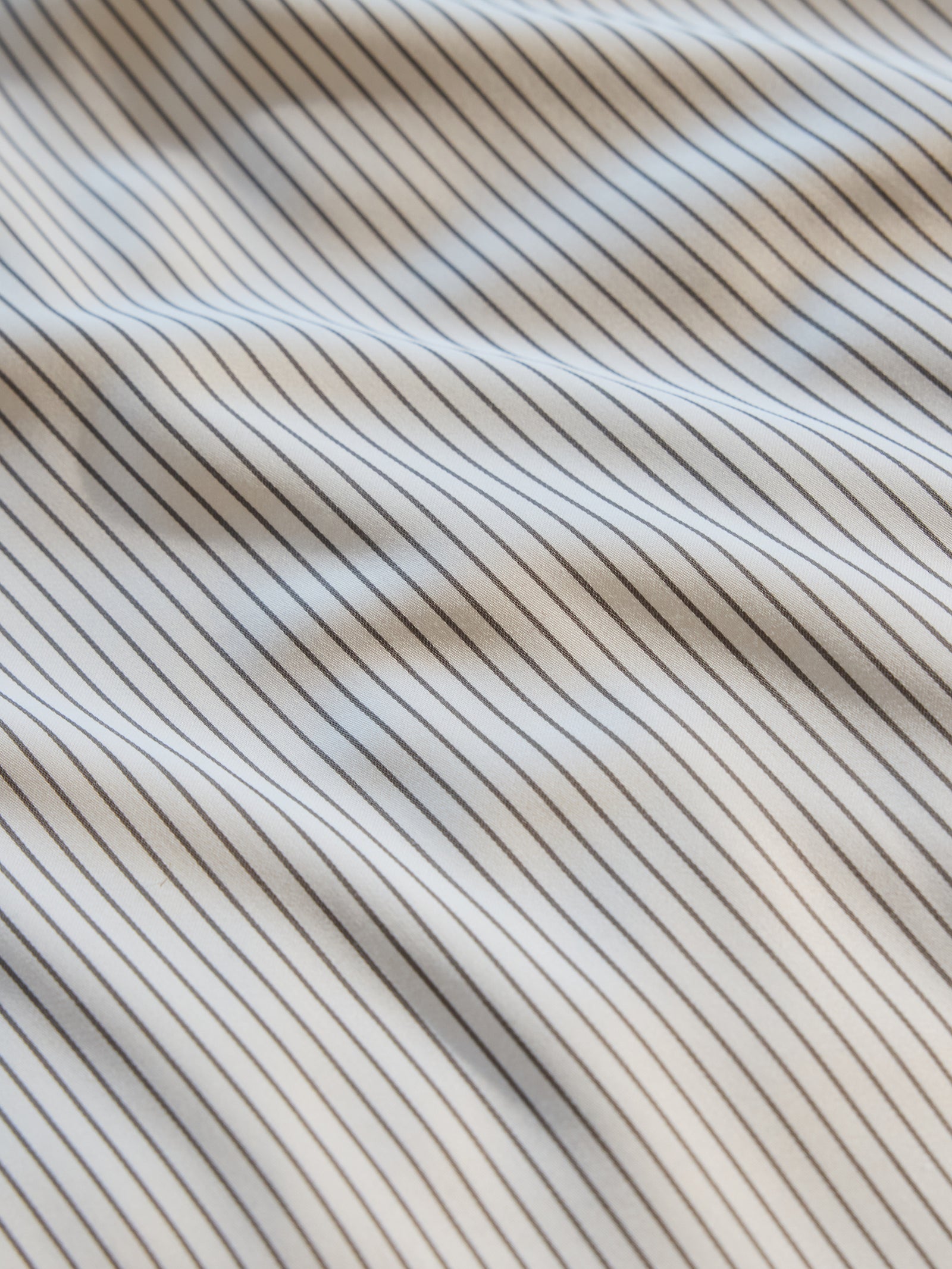 Close-up of Cozy Earth's Bamboo Flat Sheet, featuring thin, evenly spaced vertical black stripes on a white background. The material is slightly wrinkled, creating a textured appearance. 