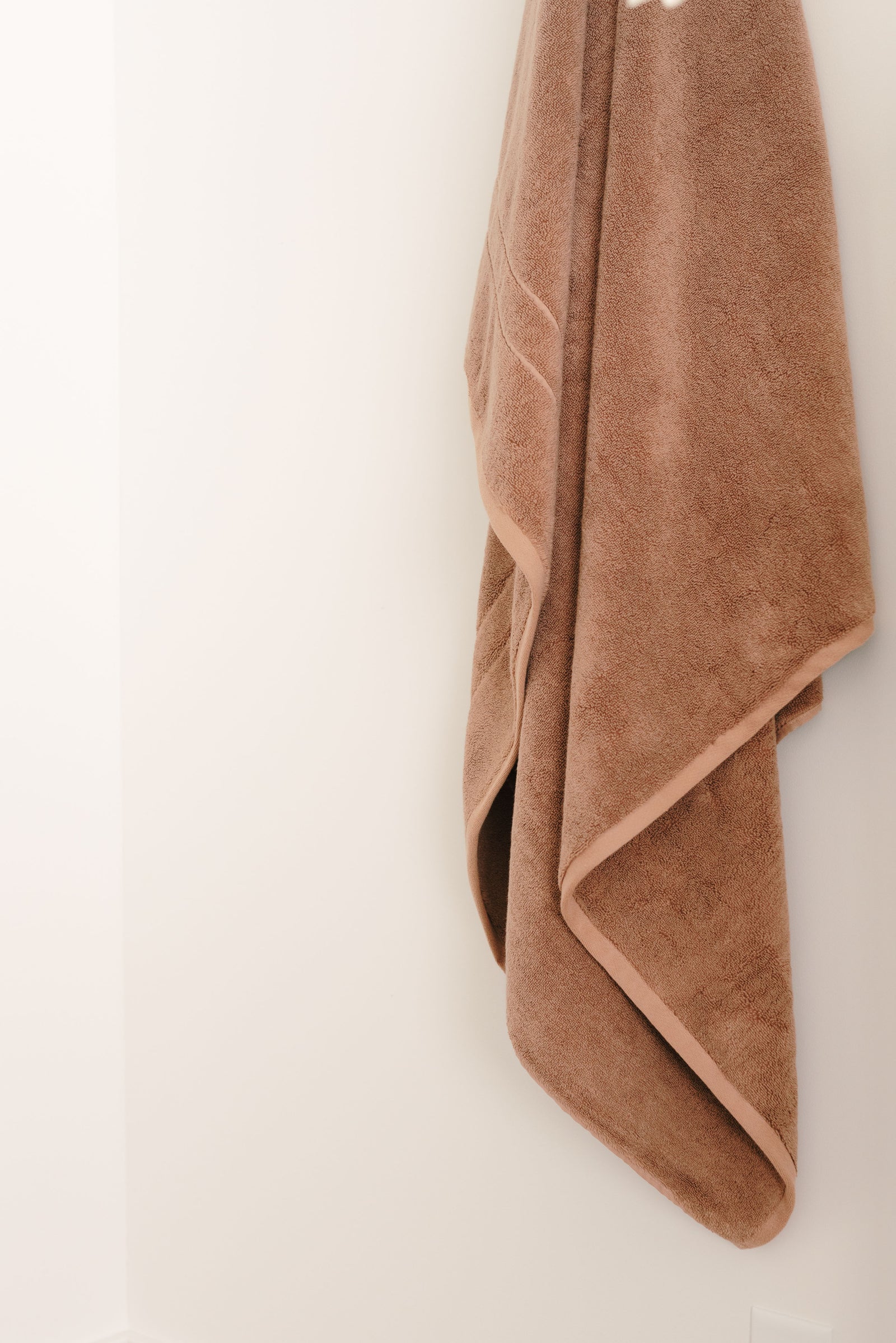 Premium Plush Bath Towel in the color clay hung on a white wall. 