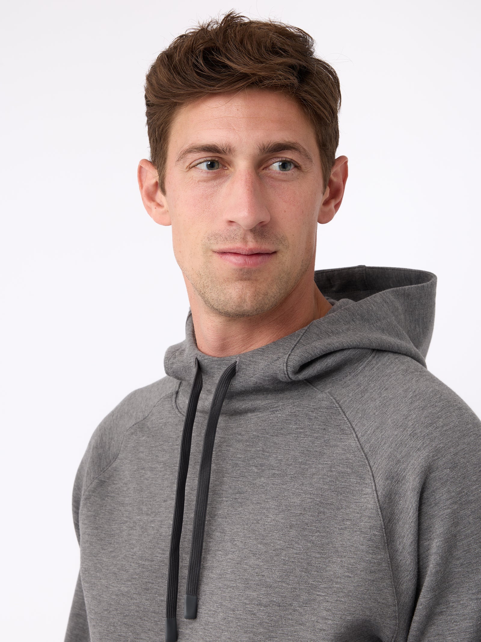 A person with short brown hair is wearing a Cozy Earth Men's StretchTech Hoodie and looking slightly to the side against a plain background. 