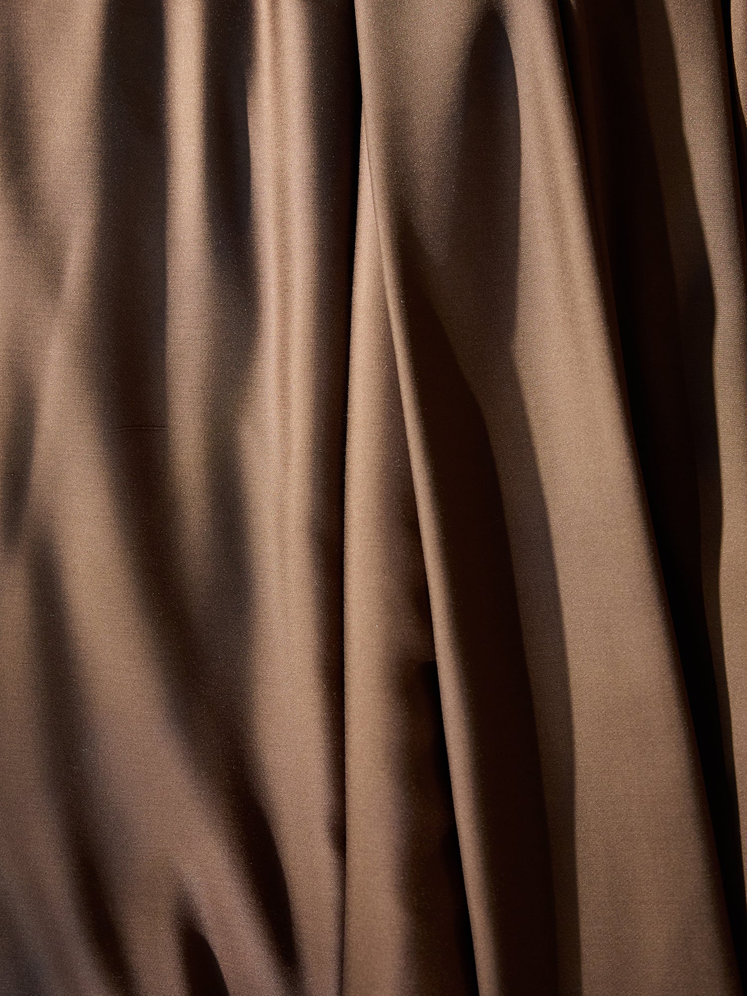 Close-up of Cozy Earth's Bamboo Flat Sheet in smooth, dark brown fabric with folds and creases. The texture appears soft and slightly glossy, catching light to create subtle shadows and highlights. 