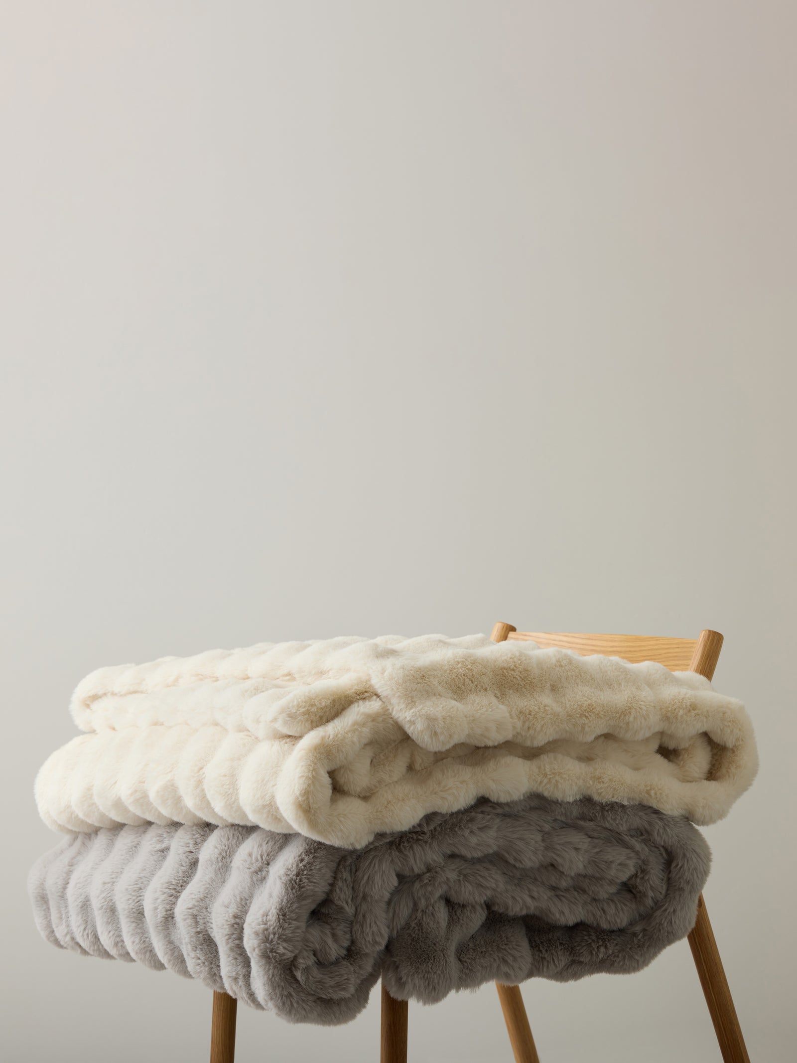 Creme and light grey lush faux fur blankets folded on top of wooden chair