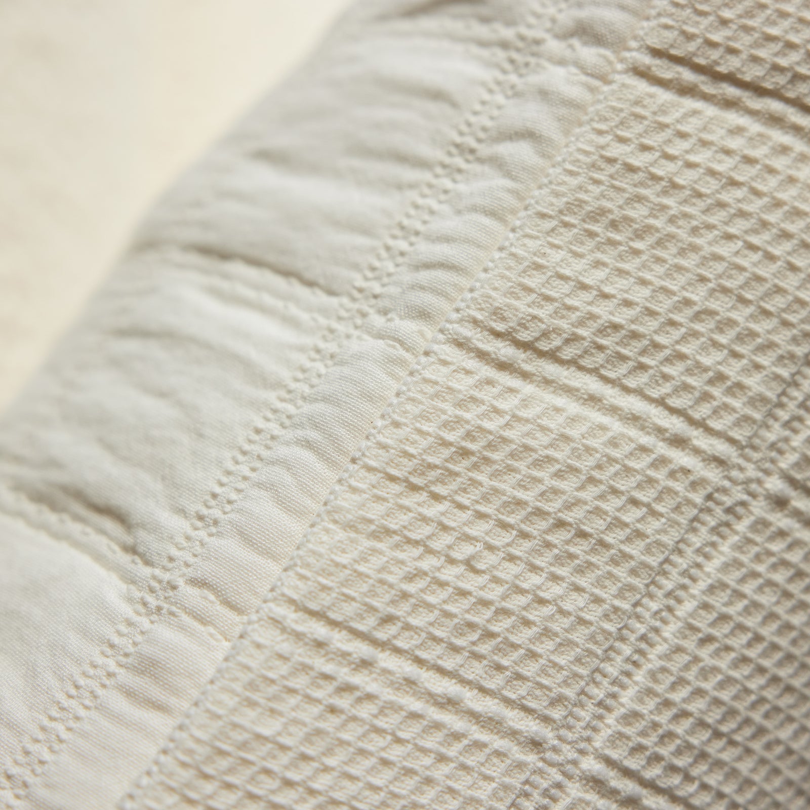 A close-up image showing the texture of the Cozy Earth Waffle Windowpane Pillow. The pillow features a beige quilted pattern with a combination of smooth and crinkled textures and stitched lines, creating a patchwork-like appearance. 