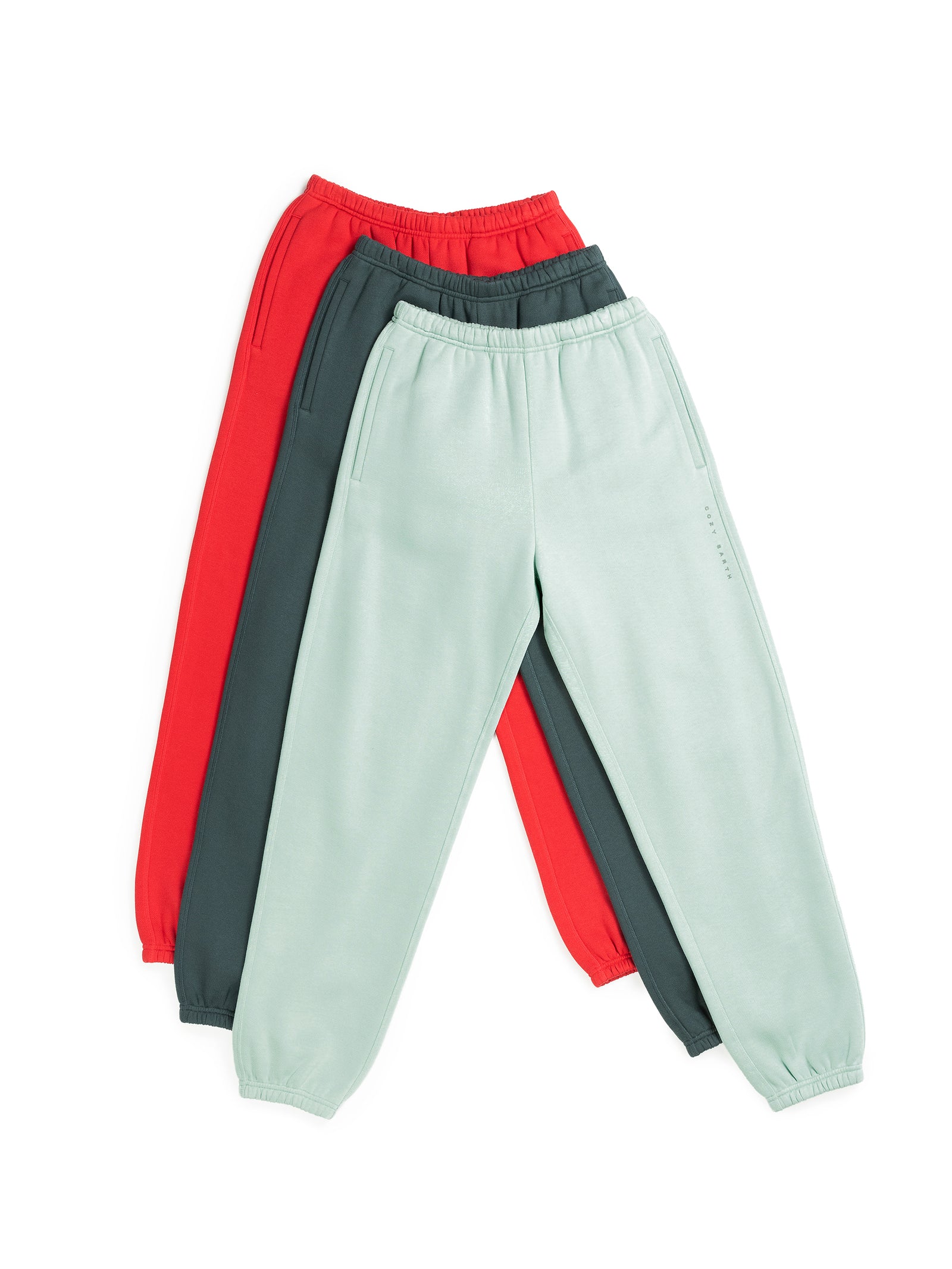 Three pairs of Men's CityScape Sweatpants from Cozy Earth in red, dark green, and light green are laid flat, stacked together. Each features an elastic waistband and cuffs, with subtle pocket details. 