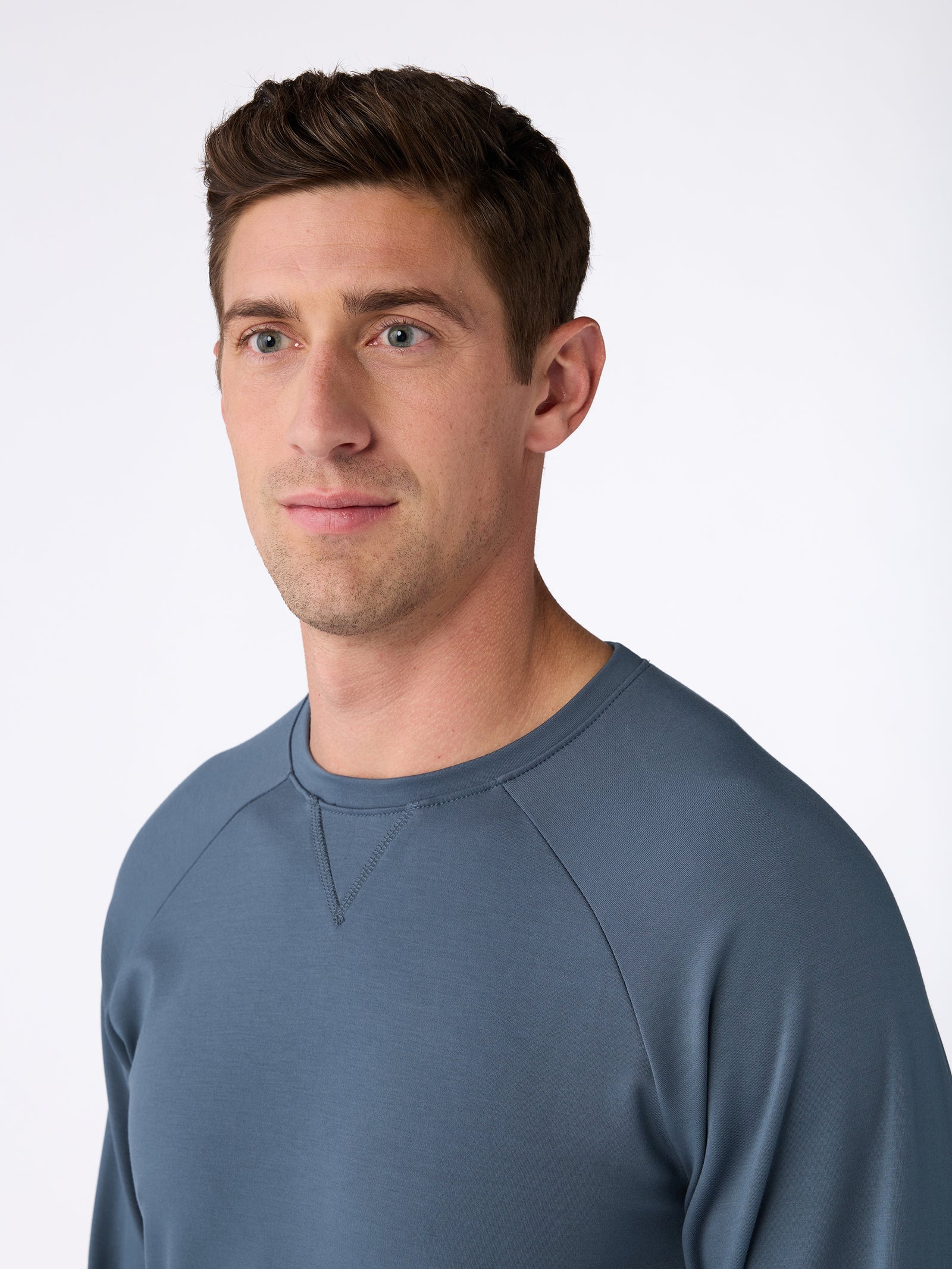 A man with short brown hair and a slight beard is wearing a Cozy Earth Men's Ultra-Soft Bamboo Pullover Crew in blue-grey. He is gazing to the side against a light background. 