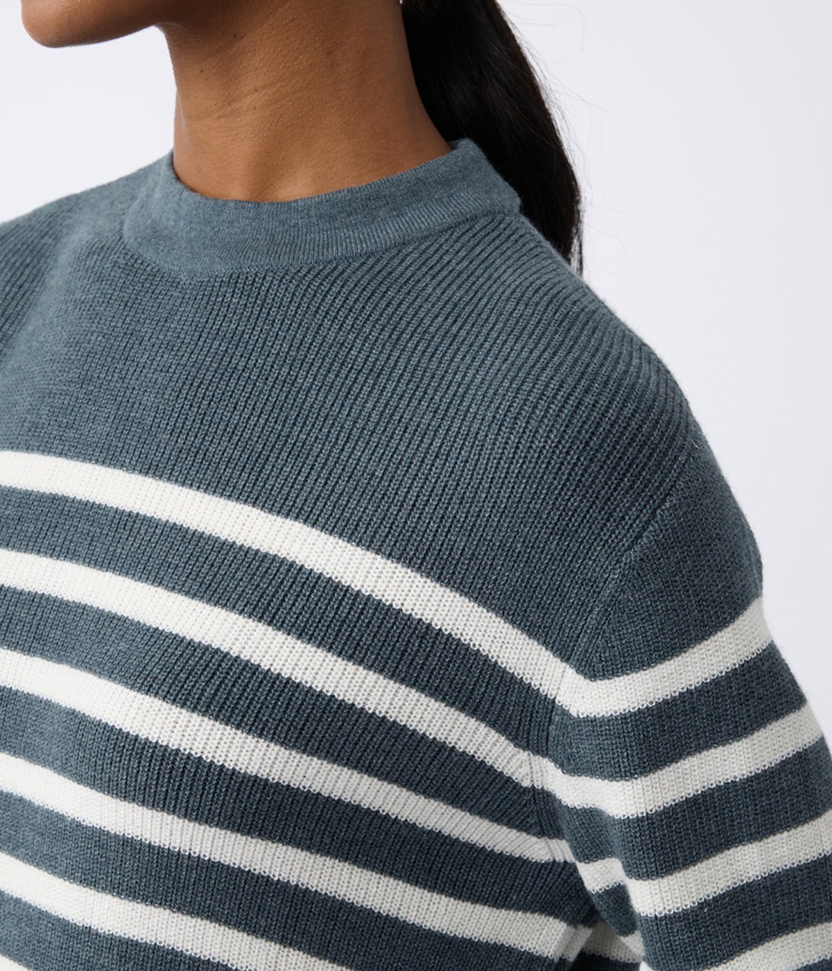 A person wears a Women's Rowan Sweater by Cozy Earth, featuring blue and white horizontal stripes with a round neckline. The person's face isn't visible against the plain white background. 