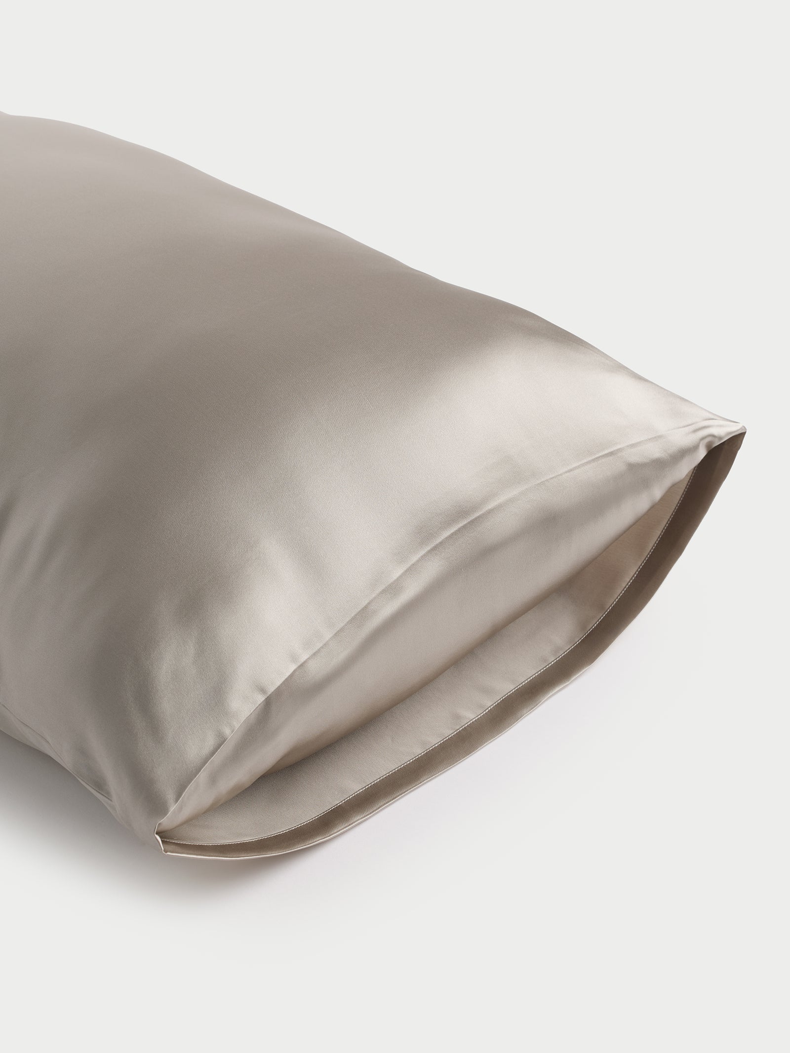 A smooth, shimmering silver Cozy Earth Silk Pillowcase is displayed against a plain white background. The fabric looks incredibly soft and luxurious, with a subtle sheen indicating its silky texture. One end of the pillowcase is slightly open. 