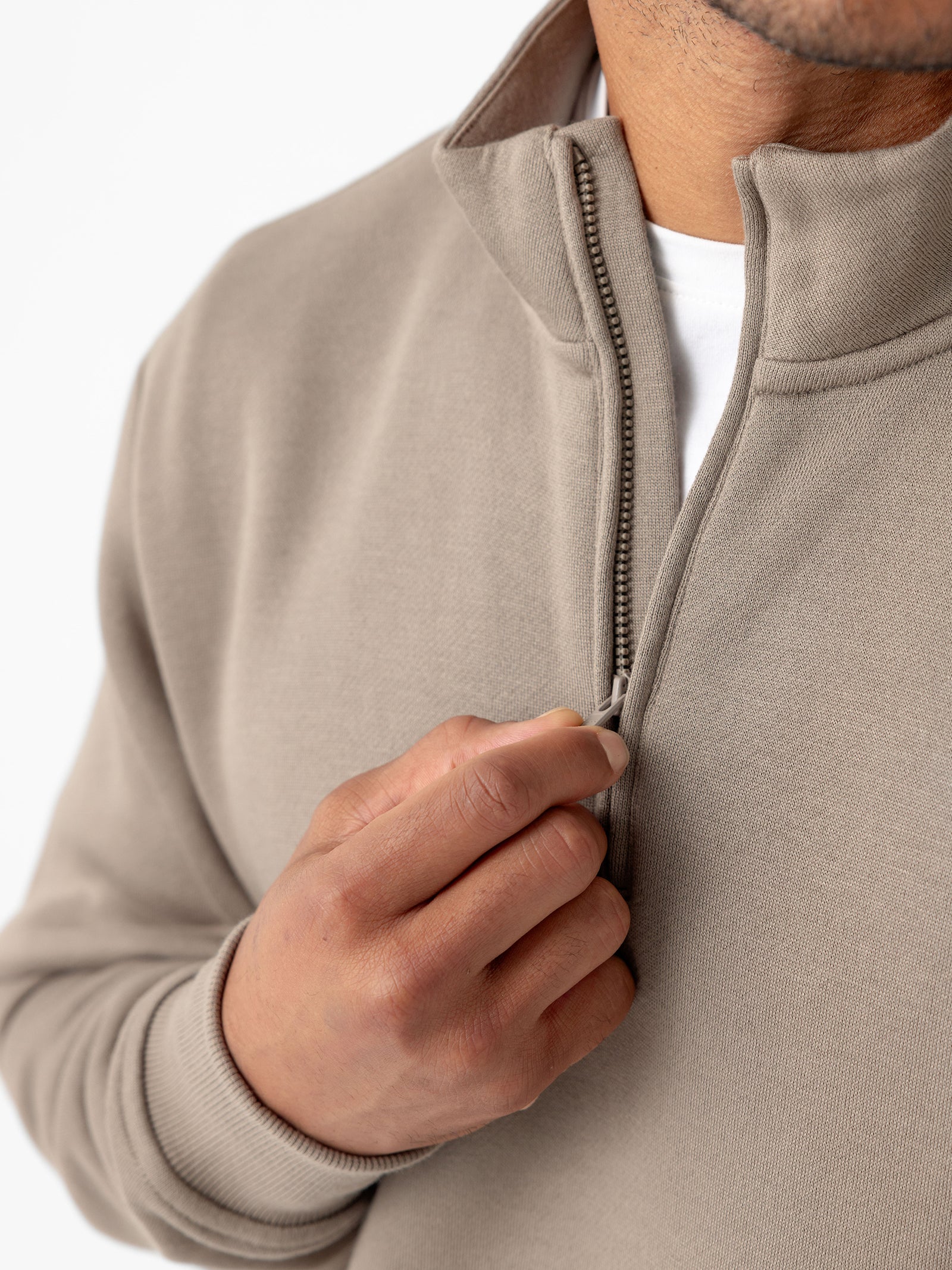 A person zips up a Cozy Earth Men's CityScape Quarter Zip in beige, revealing a glimpse of a white shirt underneath. The close-up focuses on the hand and the zipper, highlighting the texture and color of the sweater. The background is plain white. 