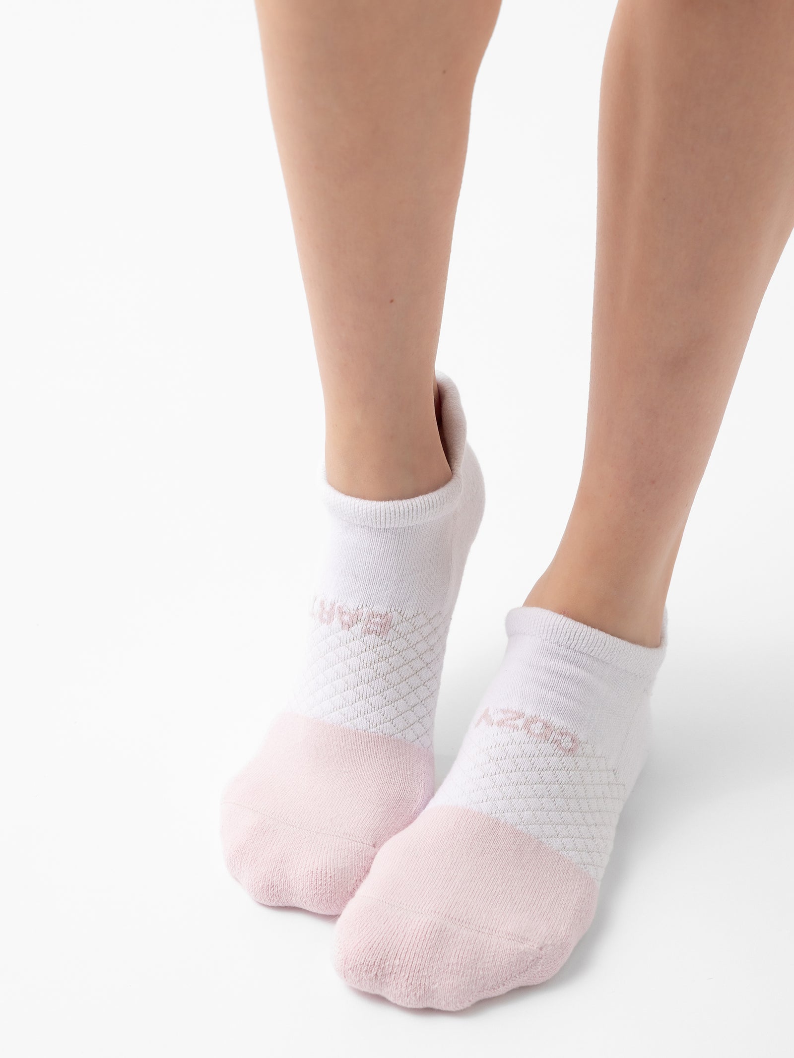 A pair of feet wearing Cozy Earth's Essentials Ankle Sock 2-Pack in white with a light pink toe area and a subtle pattern on the upper part. The background is white, and the image focuses on the socks and lower legs. 