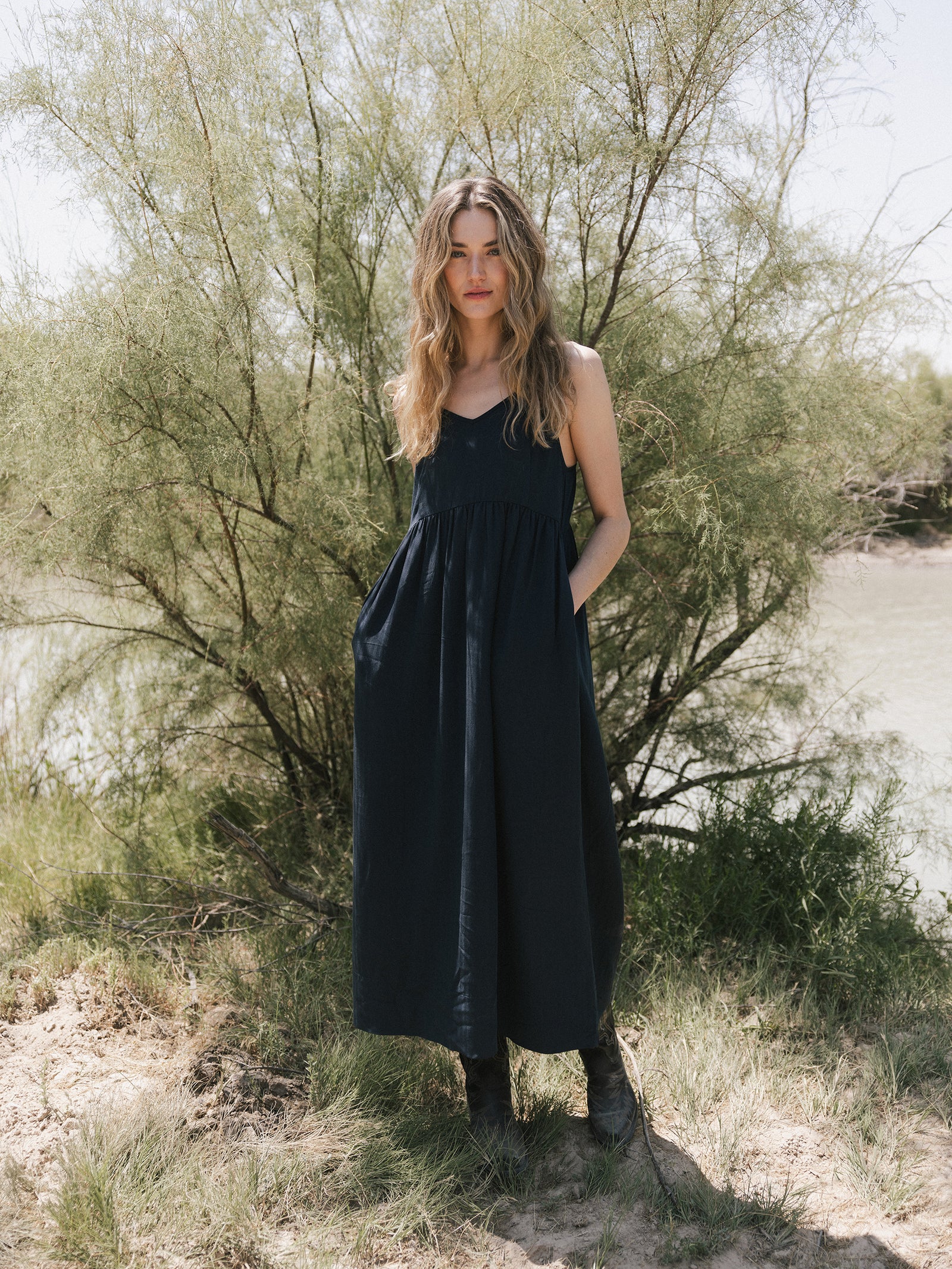 A woman wearing the Women's Sunset Gathered Dress by Cozy Earth standing in front of a tree. 