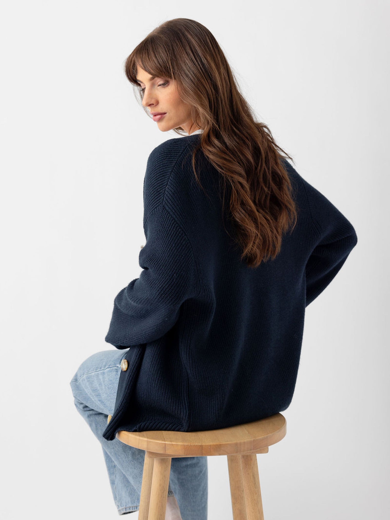 Back of woman in eclipse cardigan sitting on wooden stool 