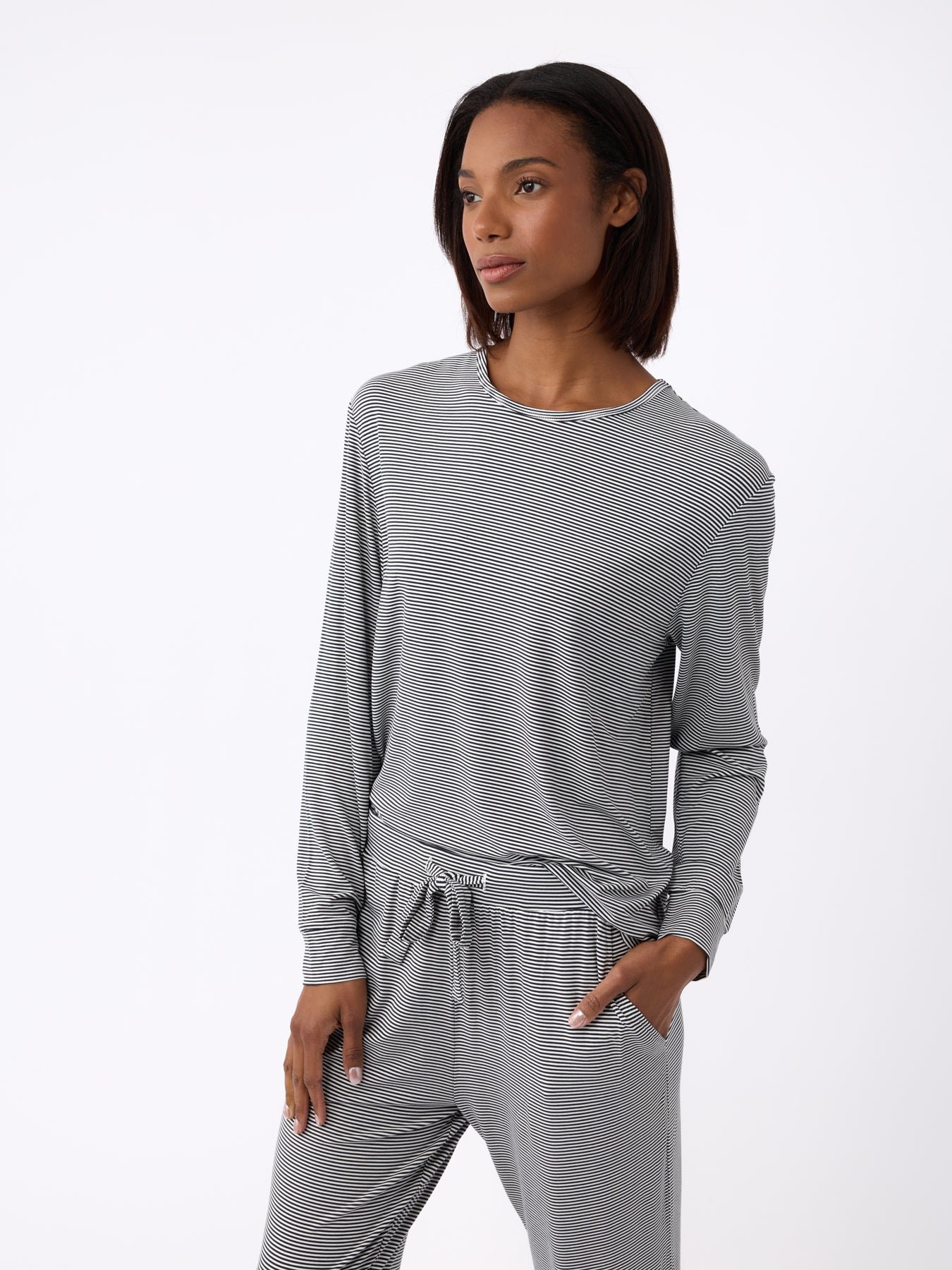 A person in a Cozy Earth Women's Bamboo Stretch-Knit Long Sleeve Lounge Tee and matching pants stands with one hand in their pocket against a white background. |Color:Eclipse Mini Stripe