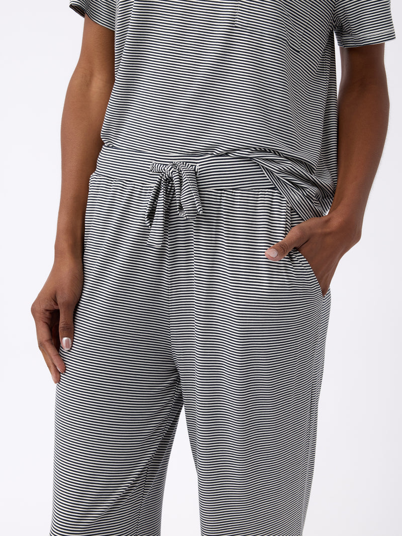 A person is wearing a gray and white striped, short-sleeve shirt with a tied waist, paired with Cozy Earth's Women's Bamboo Stretch-Knit Pant. Their hands are in their pockets against a plain white background.