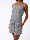 A person in Cozy Earth's Women's Bamboo Stretch-Knit Lounge Tank, a sleeveless gray and white striped romper with pockets, stands against a plain white background. The soft, comfortable fabric complements the casual pose with one hand in a pocket. |Color:Eclipse Mini Stripe