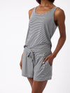 A person in Cozy Earth's Women's Bamboo Stretch-Knit Lounge Tank, a sleeveless gray and white striped romper with pockets, stands against a plain white background. The soft, comfortable fabric complements the casual pose with one hand in a pocket. |Color:Eclipse Mini Stripe