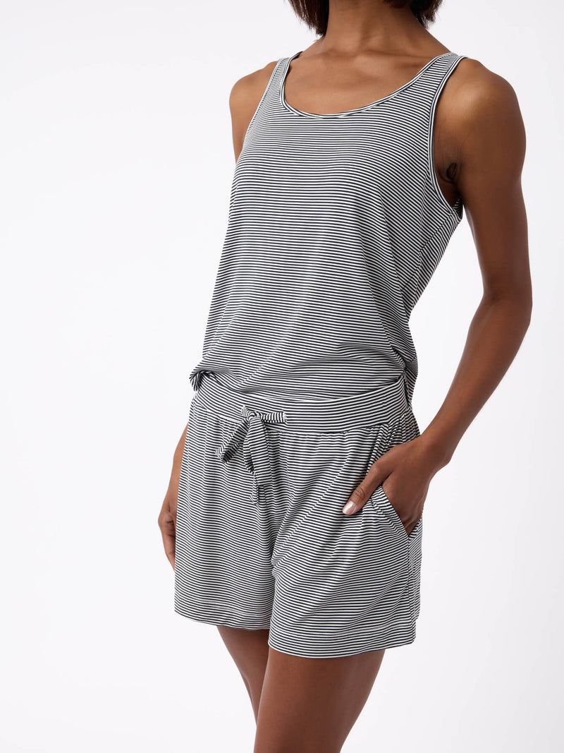 A person in Cozy Earth's Women's Bamboo Stretch-Knit Lounge Tank, a sleeveless gray and white striped romper with pockets, stands against a plain white background. The soft, comfortable fabric complements the casual pose with one hand in a pocket.