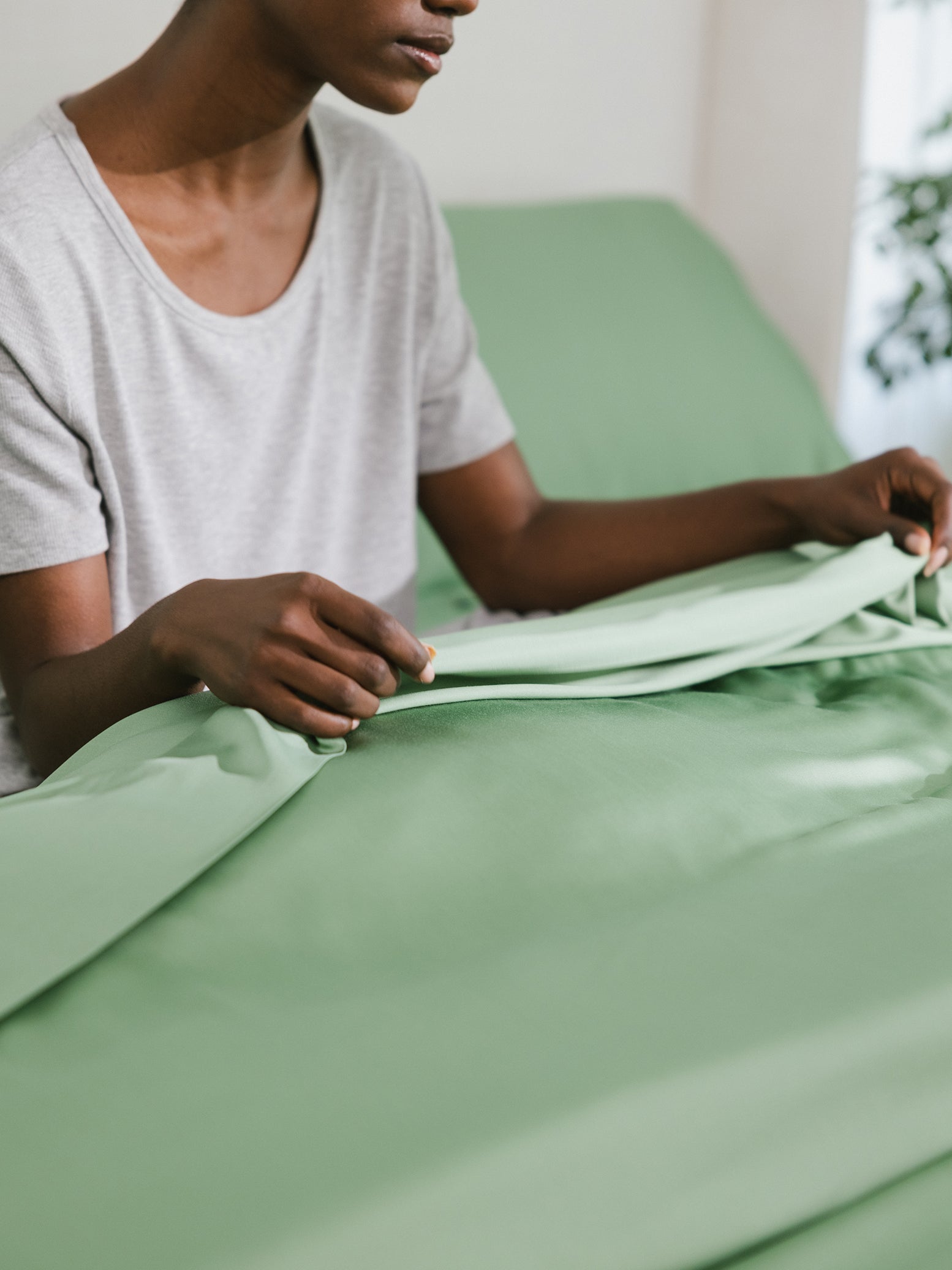 Women sitting in bed feeling the texture of the fern colored sheet 