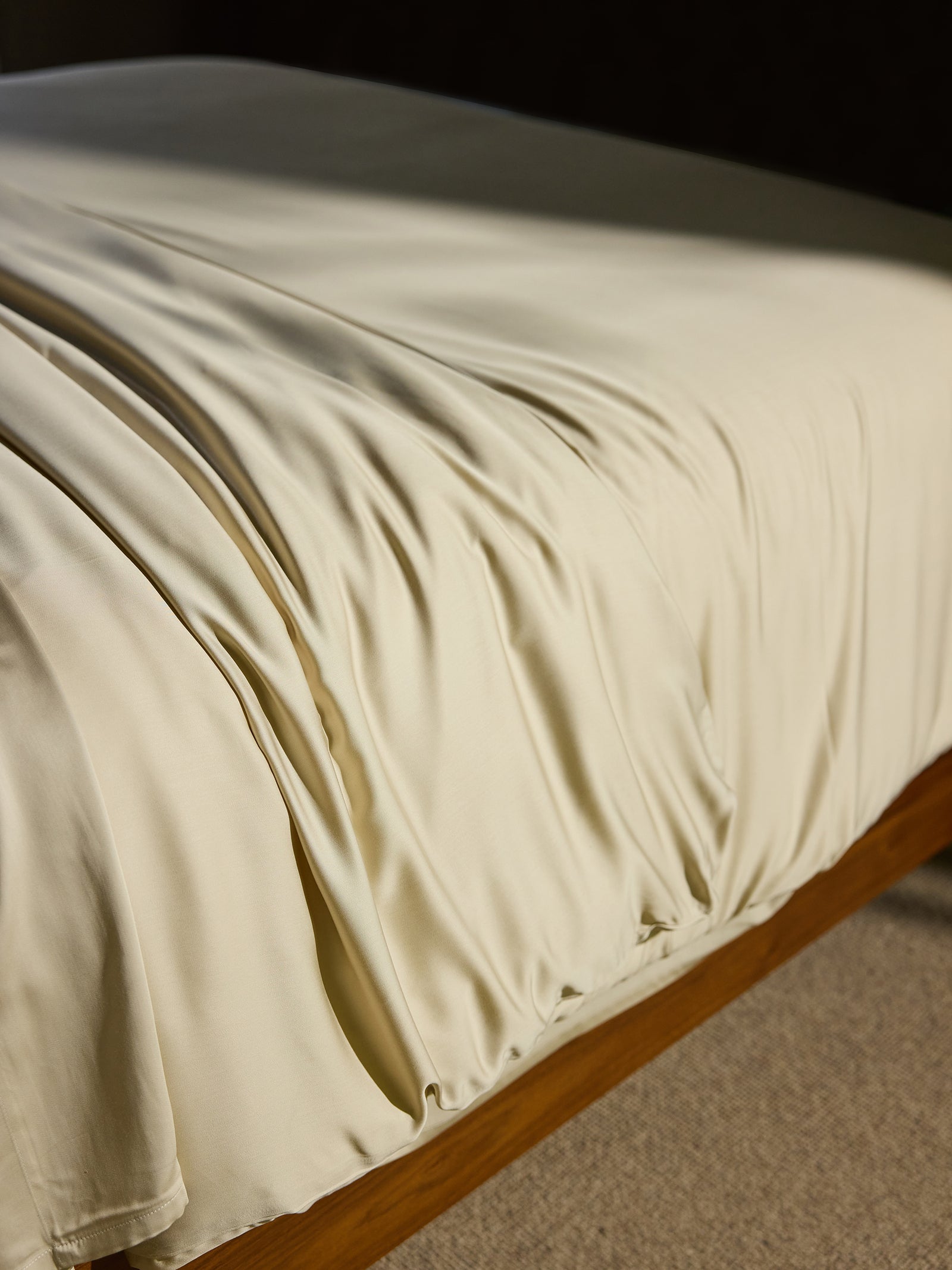 A close-up shot of a bed adorned with a Bamboo Duvet Cover by Cozy Earth, draped smoothly over a wooden bed frame. The duvet cover's lustrous texture and slight draping create soft folds, highlighting its luxurious and silky appearance. 