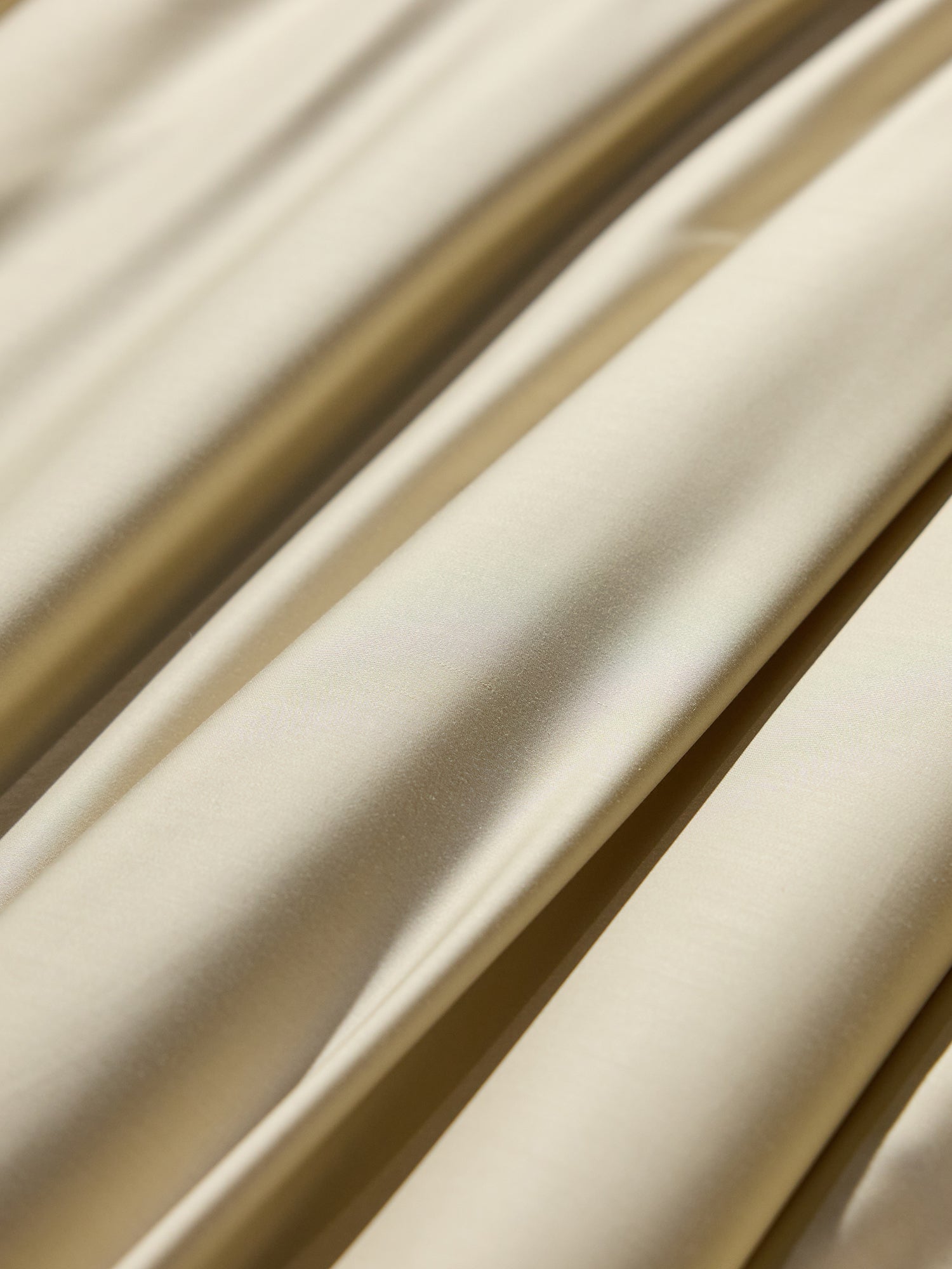 A close-up image of smooth, folded Cozy Earth Bamboo Flat Sheet in a subtle beige shade. The folds create gentle shadows, highlighting the material's soft and silky texture. 