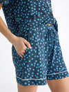 A person is wearing Cozy Earth's Women's Bamboo Stretch-Knit Short Sleeve Pajama Set featuring a blue and white floral pattern, white piping, a button-up top, and shorts, with one hand tucked in the pocket. |Color:Forget Me Nots
