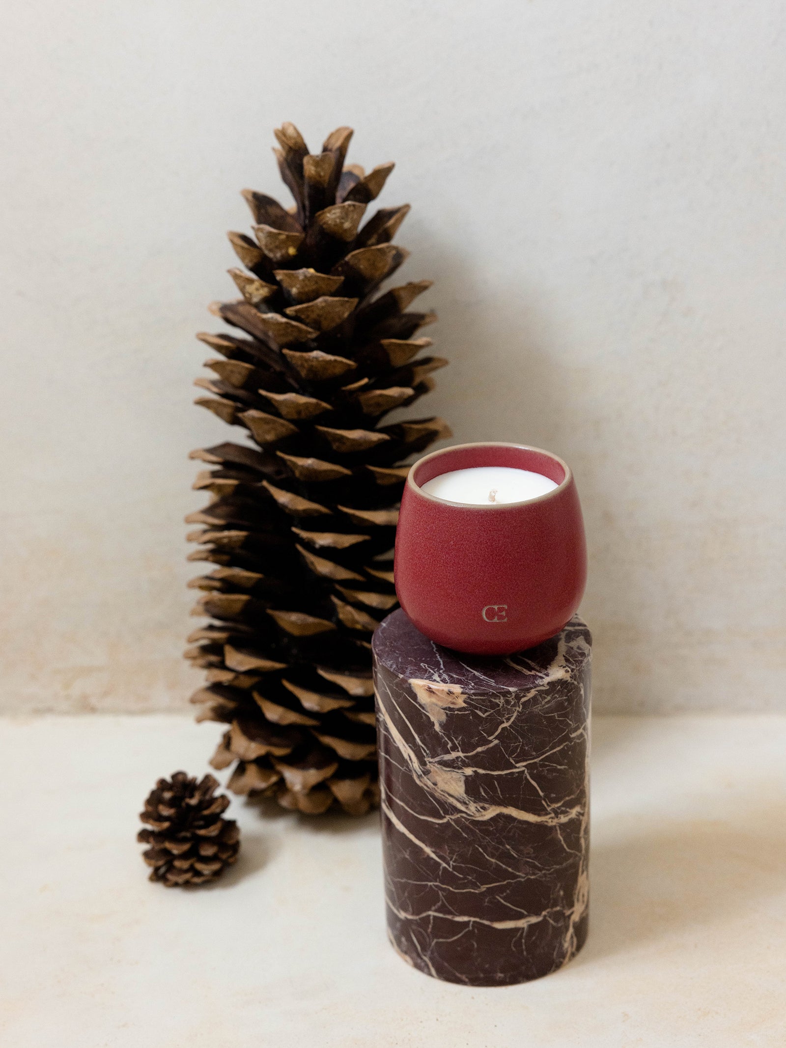 Cozy Earth Gather Candle sits on a pedestal near pinecones