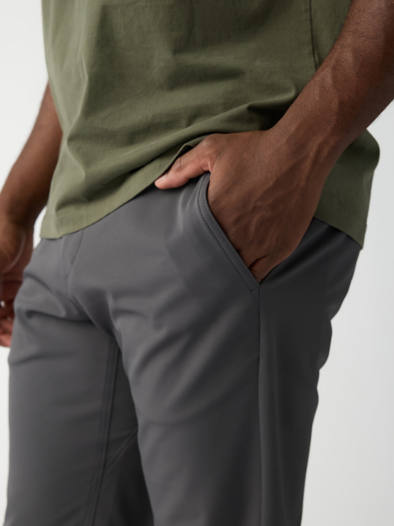 A person wears the Men's Everywhere Pant in gray by Cozy Earth and a green shirt, standing with one hand in a pocket while the other arm hangs by their side. The image highlights the texture and fit of these stylish pants. 