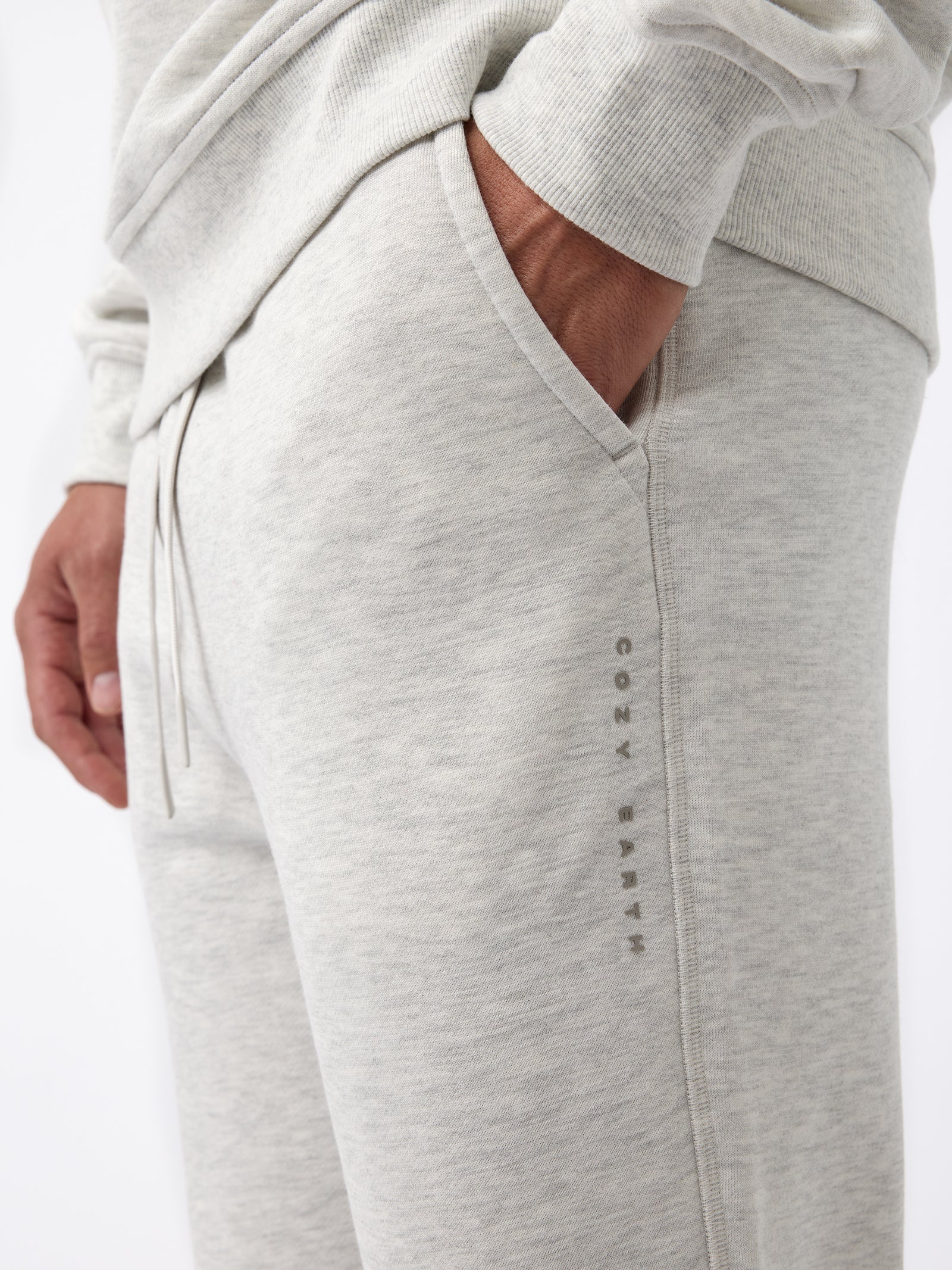 A person wearing Cozy Earth's Men's CityScape Jogger in light gray with their hand in the pocket. The joggers feature a subtle logo or text running vertically down the side and the fabric appears soft and comfortable. 