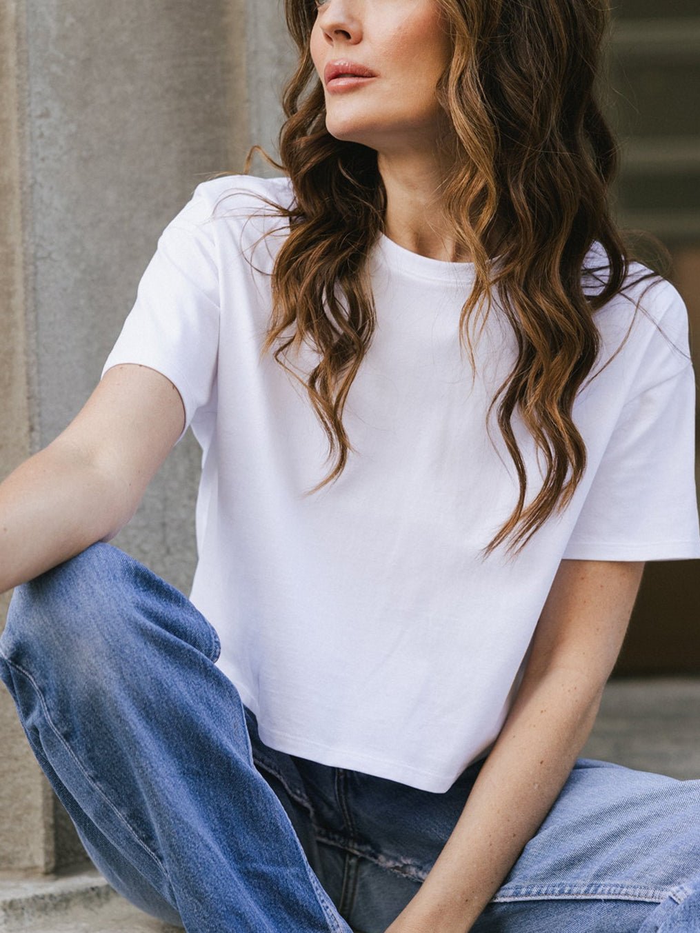 White All Day Cropped Tee. The photo of the All Day Cropped Tee is taken with a with a city style background and is worn by a woman. |Color:White