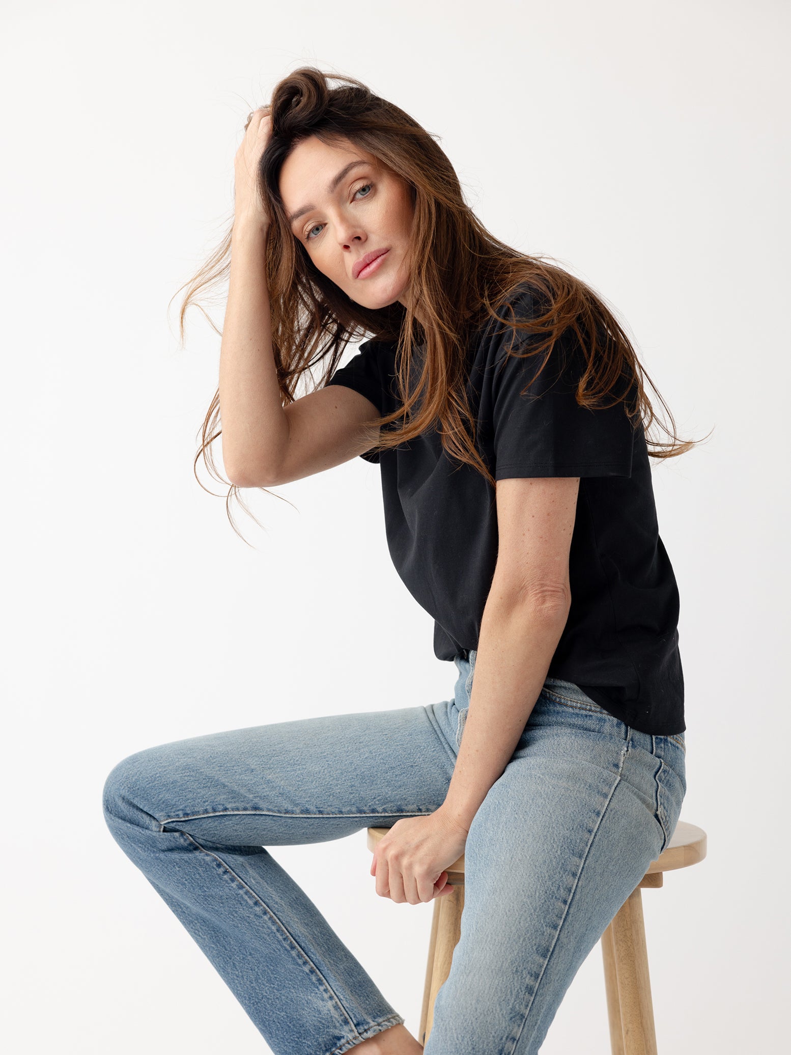 Woman sitting on stool wearing black tee and jeans 
