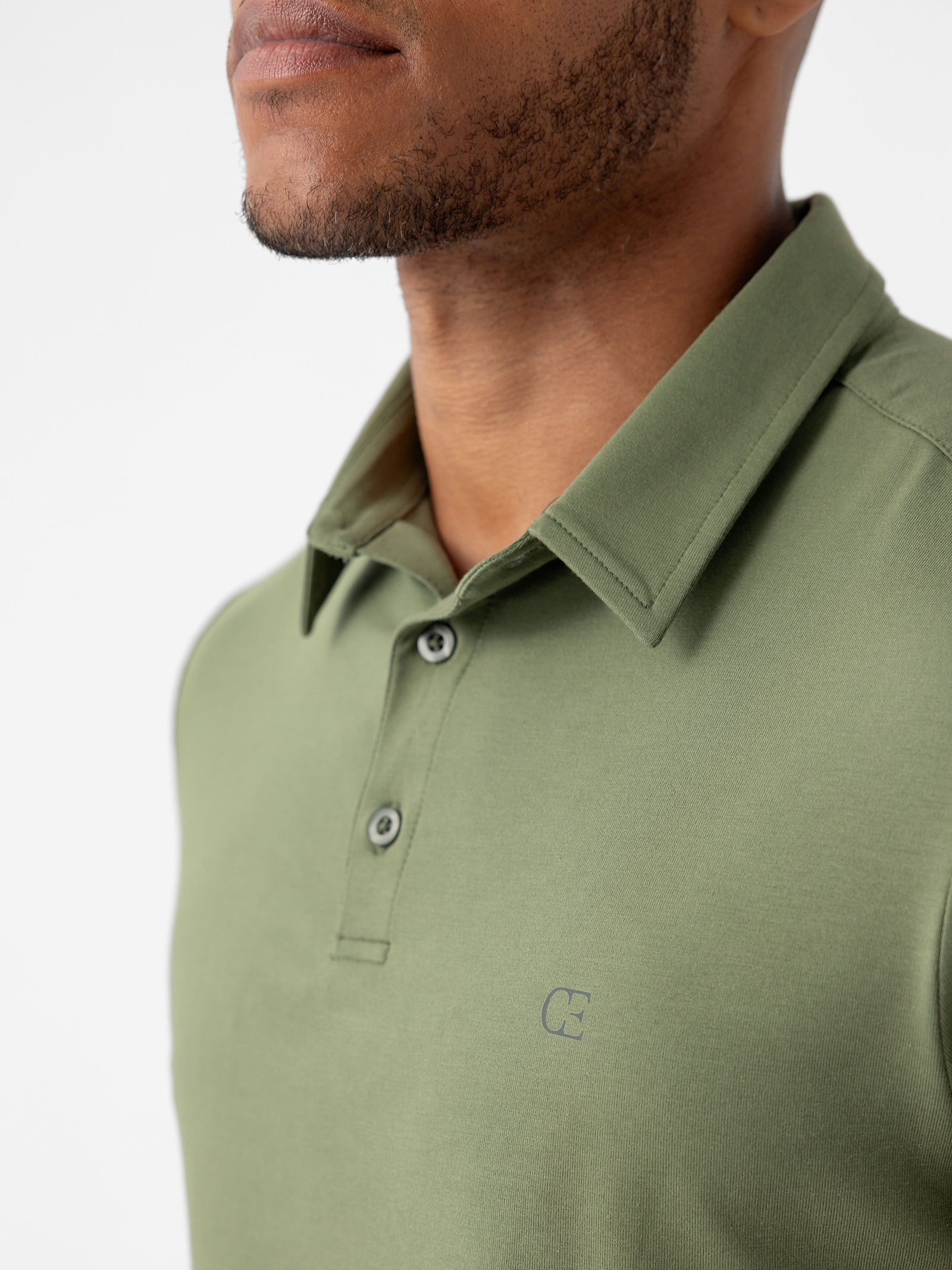 A man wearing Cozy Earth's Men's Everyday Polo in green, featuring a collar, buttons, and a small logo on the chest, set against a plain white background. 