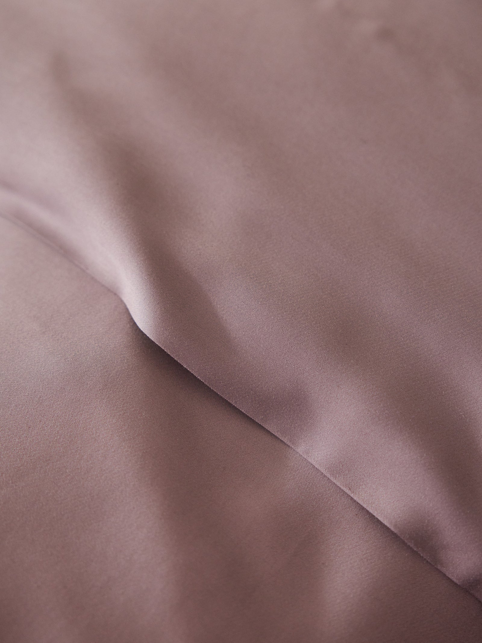 A close-up of the Bamboo Flat Sheet by Cozy Earth shows its smooth, rumpled mauve fabric with soft folds creating gentle shadows on its surface. 