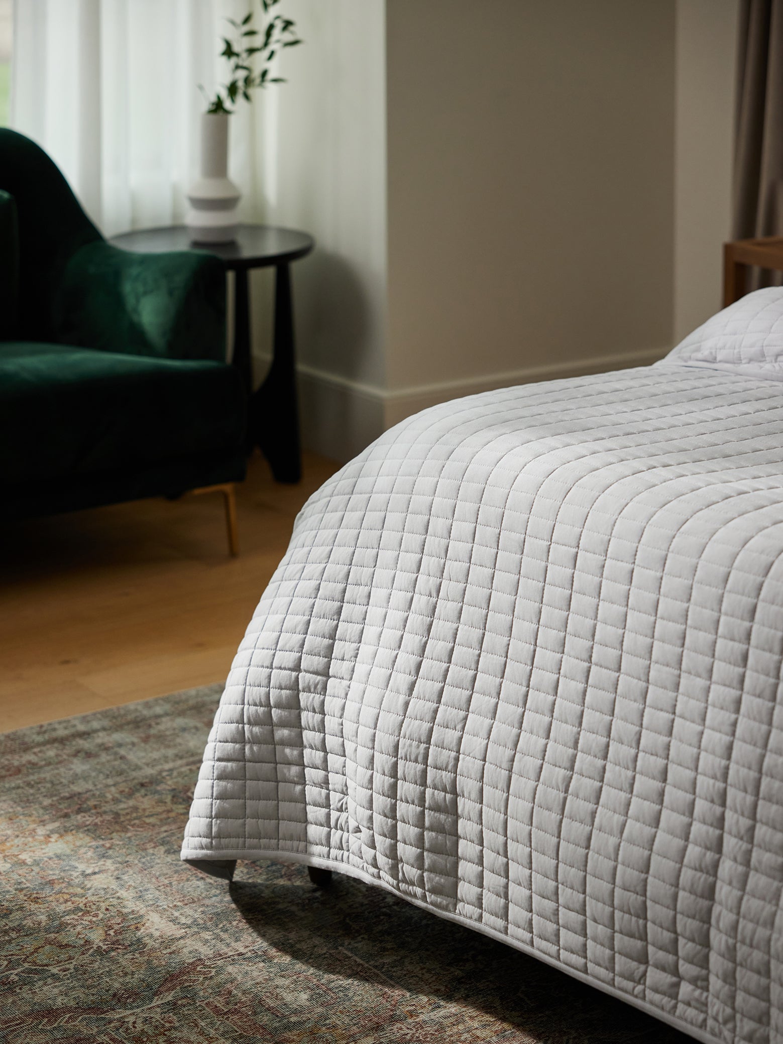 Corner of bed with draping light grey bamboo jersey quilt 